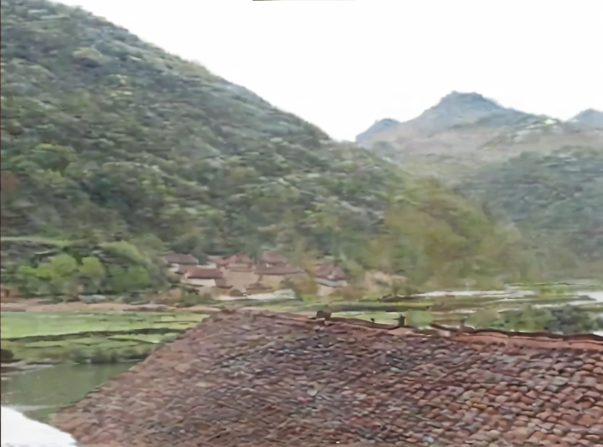 there is a man standing on a roof looking out at a valley, view of villages, of a small village with a lake, village in the background, village, chinese village, old village in the distance, behind a tiny village, with village, japense village in background, distant town in valley and hills, small village, hills in the background, low quality footage