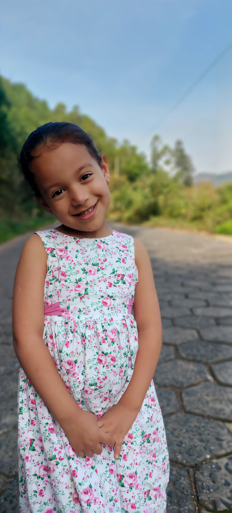 there is a that is standing on a brick road, cute young girl, she is smiling and happy, smiling girl, young girl, beautiful and smiling, dressed in a flower dress, sweet smile, 7 0 mm portrait, she is smiling and excited, she is smiling, alanis guillen, lovely smile, happy girl, wearing pink floral gown, sem alterar caracteristicas do rosto, 4k, permenecer visual