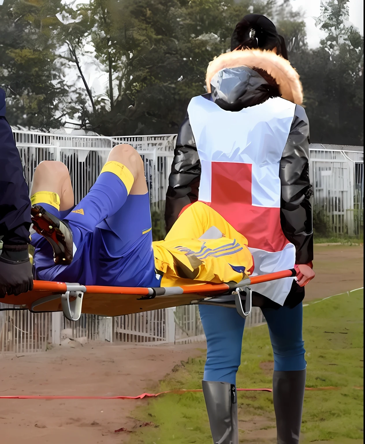 there is a male soccer player in short sportswear lying injured on a stretcher, there is an injured sportsman who is covering his face on a stretcher, an injured sportsman is covering his face with his hands, an injured sportsman is writhing ecstatic in pain on a stretcher, dramatic pity pose, there is a very female woman in a high-shine coat, a high-shine black wetlook coat, a long shiny coat, a wetlook glossy coat, a wet black laquered coat, a very female looking wife is wearing a wetlook coat, injured, medic, soccer action pose, affection pose, lecherous action pose, dramatic action pose, theatralic pose, there is an attractive woman that is carrying a suffering man on a stretcher, there is a beautiful woman in a shiny coat who is carrying a blond man on a wet orange stretcher, a longhaired beautiful woman in a high-shine coat, a longhaired woman in a shiny downcoat, a woman is carrying a stretcher with a shorthaired man who is wearing shorts and a t-shirt, a weak man in spots shorts is consciousless and needs to be carried on a wetlook pvc stretcher, a shorthaired man with closed eyes is carried on a stretcher by a longhaired woman, a woman looks very scared and terrified, a consciousless man with closed eyes is suffering very much and has a very painful face, photo, photo shoot, photographed , accident, help, aid, first aid, pity