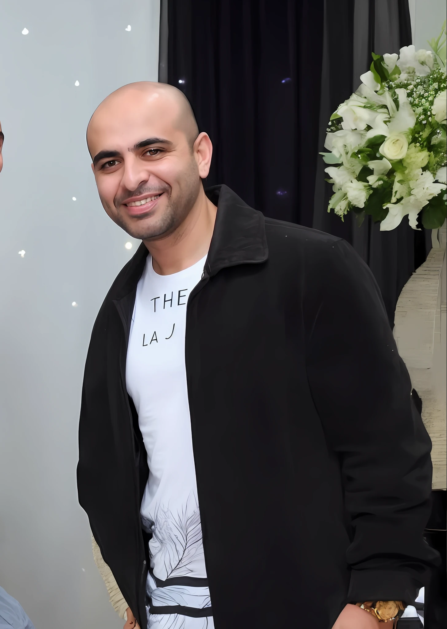 homem sorridente em jaqueta preta ao lado de um vaso de flores, Ahmad Merheb, taken in the late 2010s, um homem vestindo uma jaqueta preta, taken in the early 2020s, tiradas no final dos anos 2000, Mohamed Chahin, Sam Nassour, Elias Chatzoudis, George Doutsiopoulos