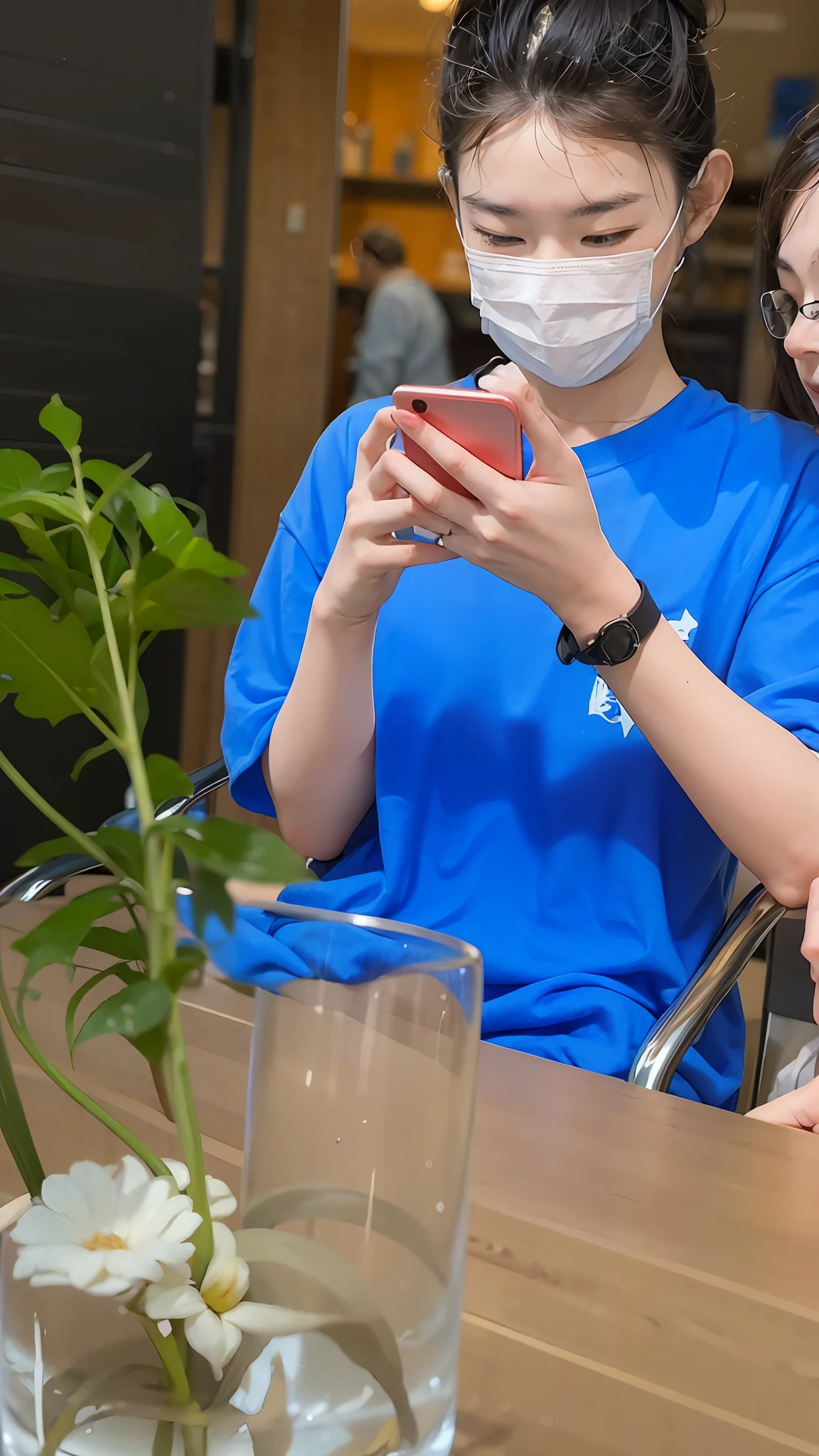 He sat at a table,In the vase is a plant, holding a smartphone, Check your phone, candid photo of, wearing face mask, he is holding a smartphone