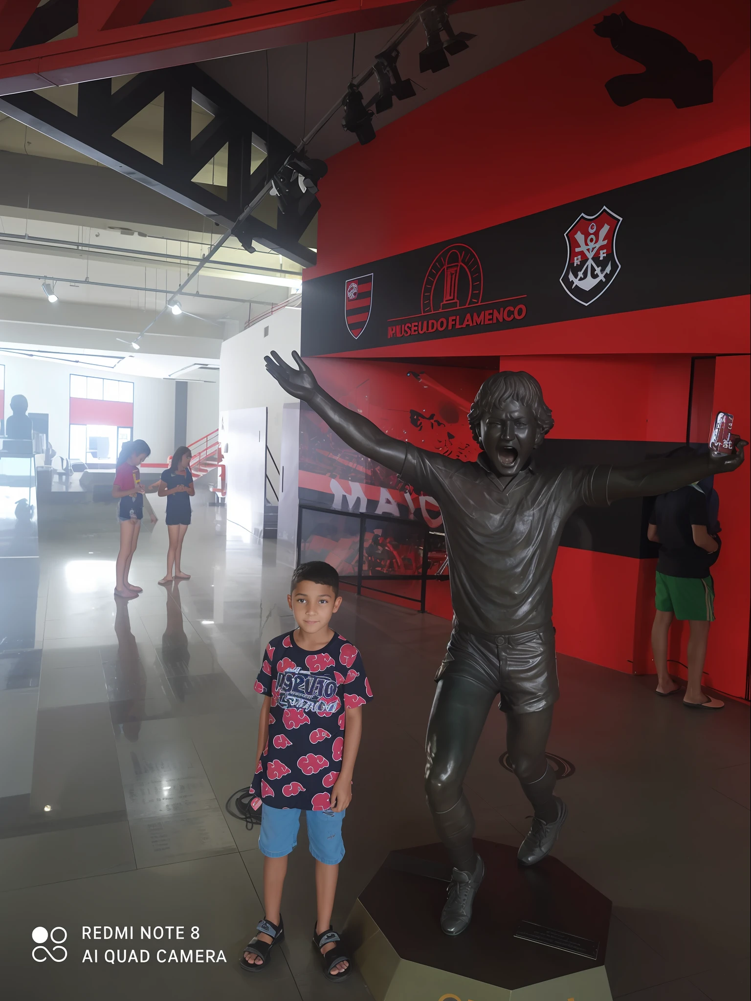 Arafed boy next to a statue of a man in a stadium, posing like a statue, inspired by Ivan Meštrović, inspired by Sava Šumanović, mateus 9 5, Lendas, cabrito, Directed by: Milton Menasco, inspirado em Oswaldo Viteri, Tomado com Sony Alpha 9, Directed by: Fernando Gerassi