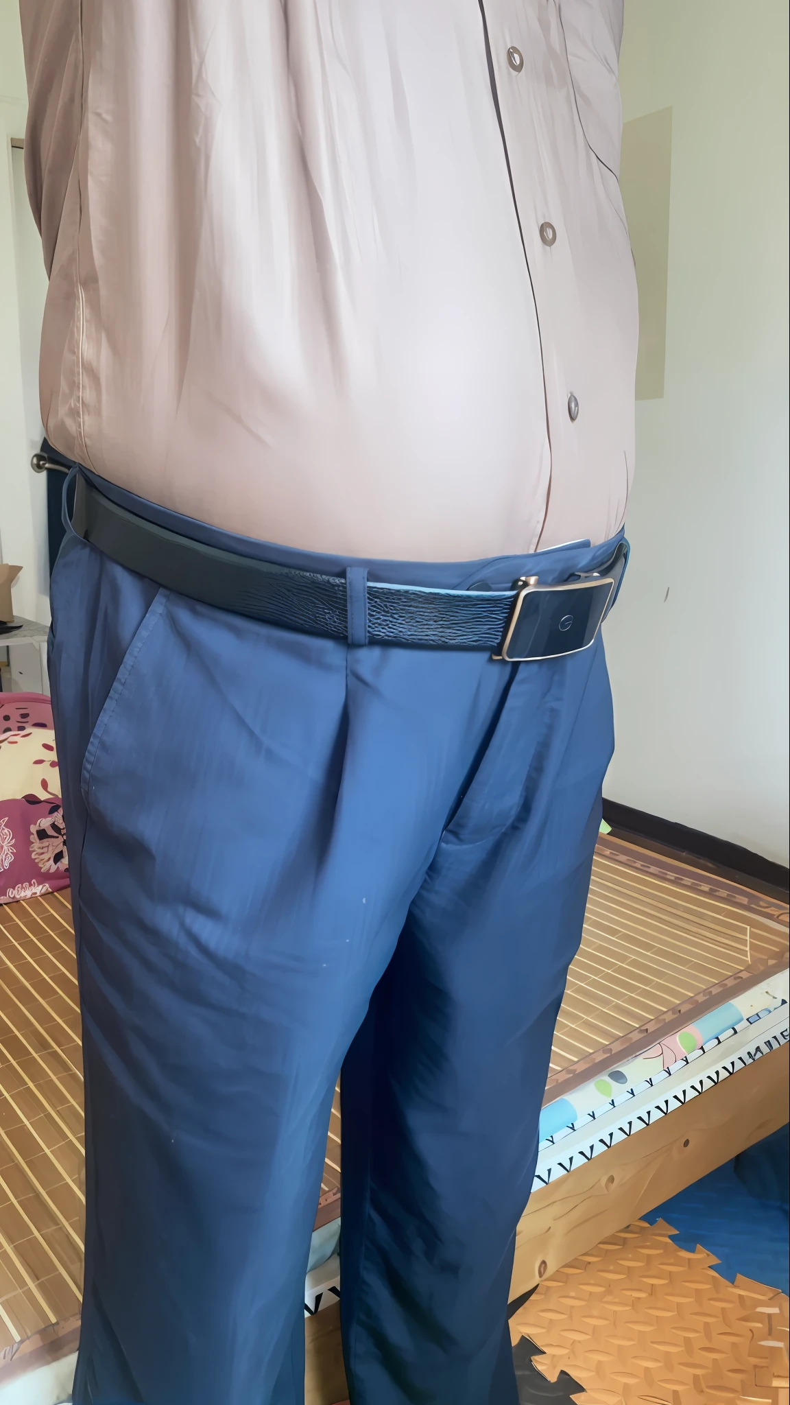 The Arad man in a tan shirt and blue pants stands on the mat, middle shot waist up, with two front pockets, hand on hips, big belt, Large pants, waist - shot, wearing pants, wearing only pants, belly, Fat belly, visible abdomen, folds of belly flab, wide belt, glass ball at the waist