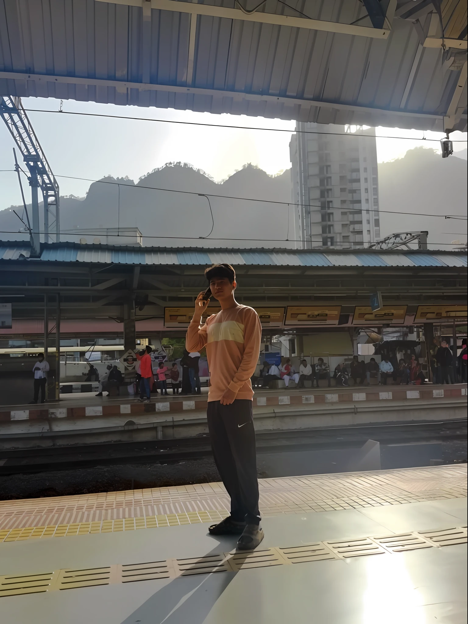 there is a man standing on the platform of a train station, with mountains in the background, moutain in background, with mountains in background, in hong kong, drinking a beer at train station, with a city in the background, at sunrise, train station, standing in front of a mountain, selfie photo, with backdrop of god rays, mountain in the background