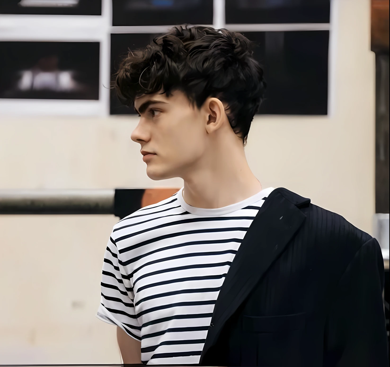 Homem de camisa listrada e jaqueta preta em frente a uma parede, Declan McKenna, Estilo de Seb McKinnon, cabelos cacheados e curtos, curls on top of his head, ele tem cabelos castanhos curtos e cacheados, miles johnstone, timothee chalamet, Juliano Ope, Elliot Alderson, Estilo de Ilya Kushinov, bladee from drain gang