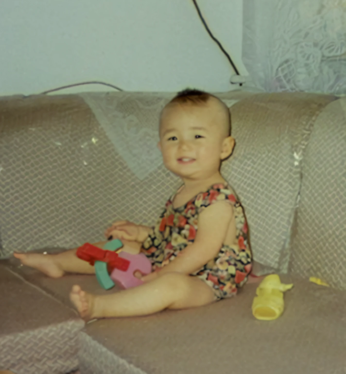 There is a  sitting on the sofa holding a toy, coloured photo, about 3 5 years old, Sitting on the sofa, he is about 2 5 years old, she is about 2 5 years old, old picture, he is about 30 years old, he is about 3 0 years old, childhood friend, He is! about 3 0 years old