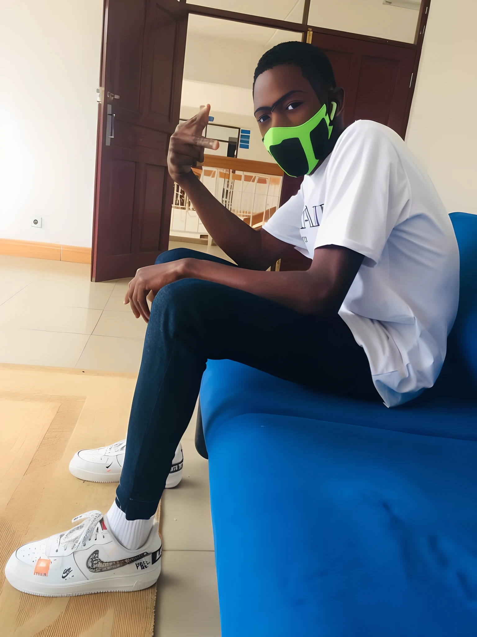 There is a man sitting on a blue couch wearing a green mask, sentar-se casualmente, com uma pose cool, Upload de alta qualidade, Sittin, Pose legal, sitting on couch, sitting on a couch, sentado em um lounge, em estilo de davey adesida, com fones de ouvido, sentado em uma cama, relaxing after a hard day, exclusivo