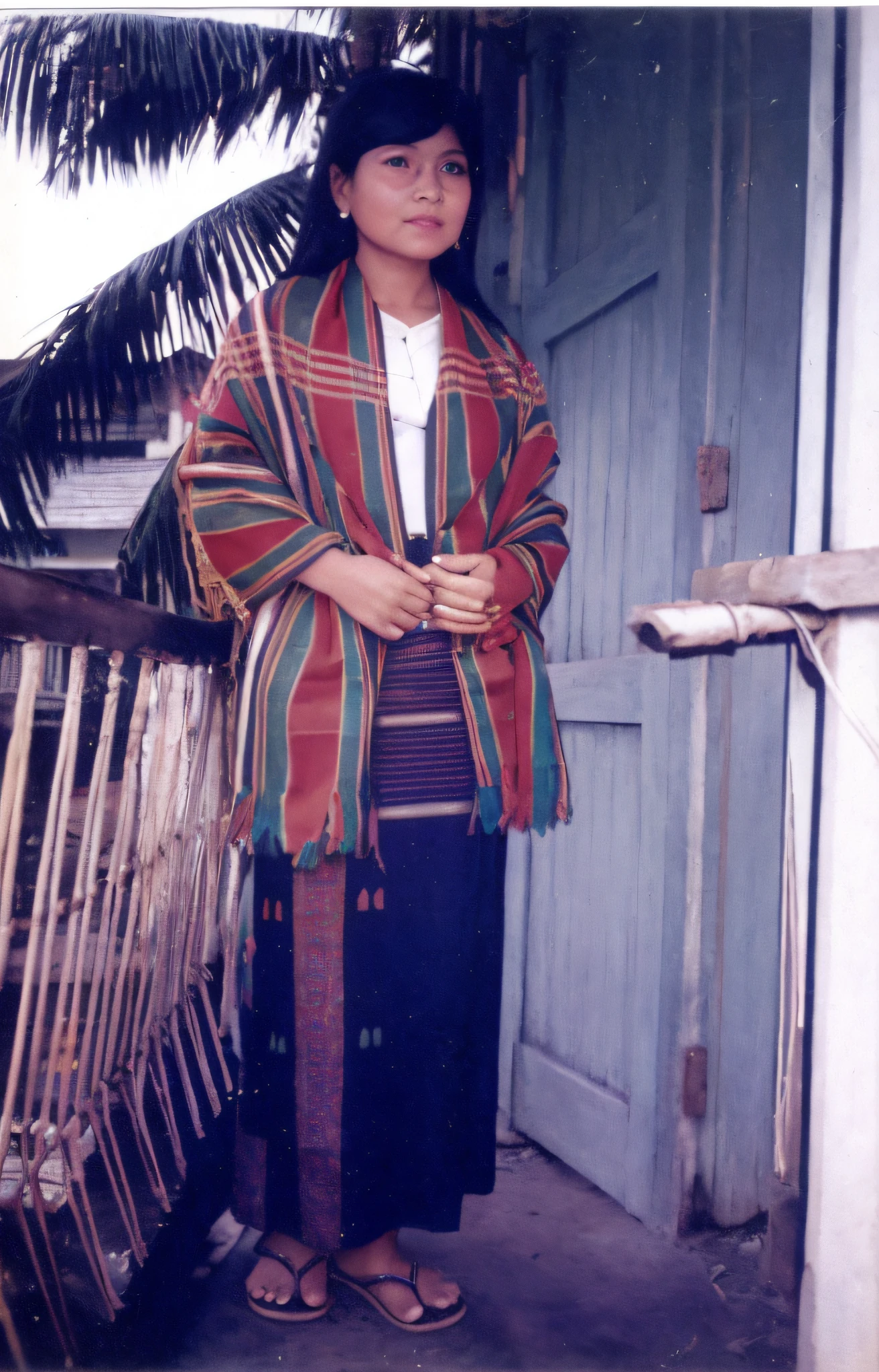 there is a woman standing outside of a house wearing a colorful blanket, wearing authentic attire, wearing traditional garb, traditional dress, traditional clothes, traditional costume, traditional tai costume, traditional clothing, around 1 9 years old, wearing bihu dress mekhela sador, photographic still, full body in shot, wearing an elegant tribal outfit, sukhothai costume