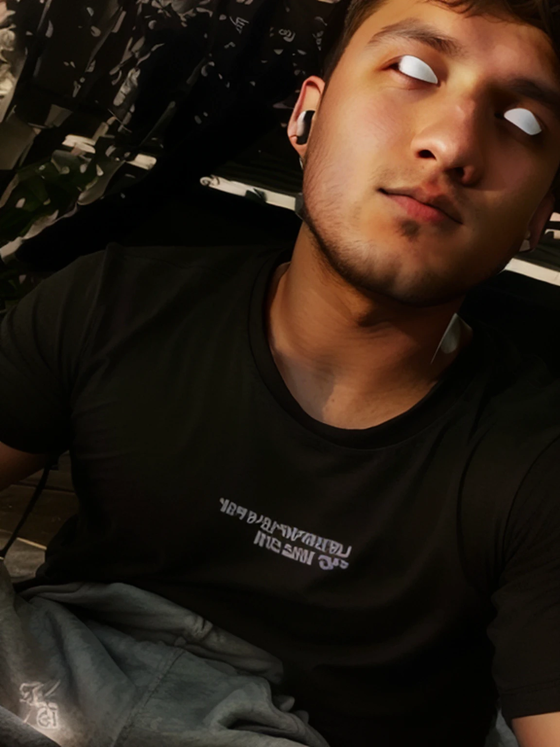 There was a man sitting outside,Bring headphones,23years old, he is wearing a black t-shirt,personal profile picture