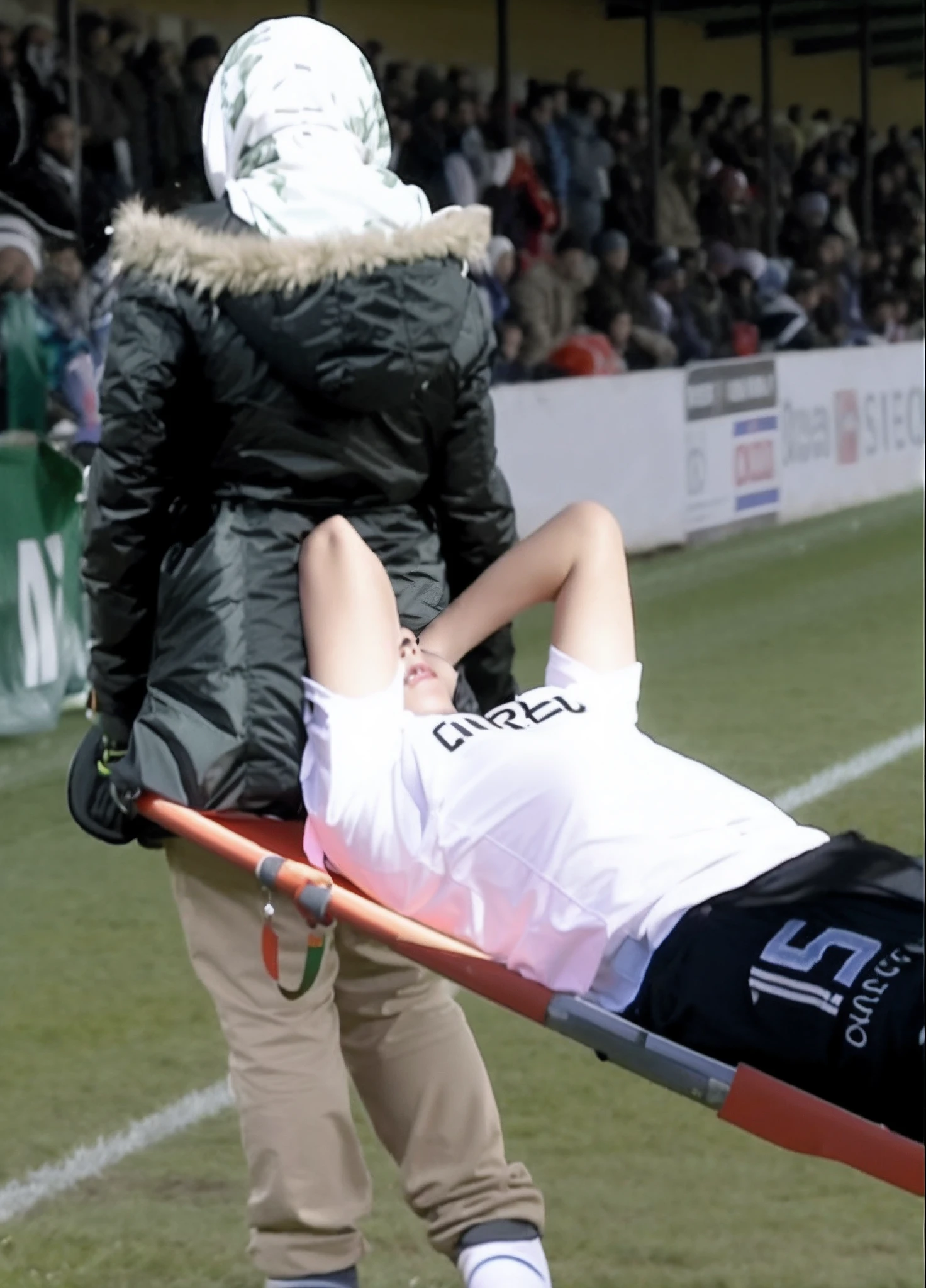 A football scene with lots of spectators, In the foreground a beautiful long-haired woman in a shiny black down coat with a horrified face is carrying an injured man in a white and blue matte sports outfit who has put a hand over his pain-distorted face from left to right out of the stadium on a shiny orange stretcher, the injured sportsman in matte white-blue sportswear is placed horizontally on the stretcher with his handcovered head to the left and the lightly angled legs to the right, the injured sportsman has his painful face close to the shiny downcoat of the beautiful woman and has placed one arm and hand over his forehead, the beautiful woman who is carrying the stretcher from left to right has a very shocked face and is shoting out with horror to us