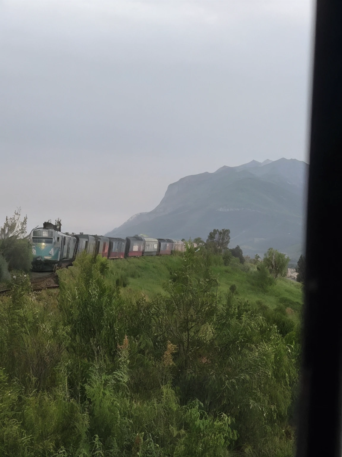 There is a train that goes on the tracks near a mountain, colinas en el fondo, A lo lejos hay una colina rocosa, Edificio en la distancia, Moutain al fondo, Vista desde la distancia, Edificios en la distancia, Vista urbana en la distancia, Visto en Perfil desde muy lejos, templo en la distancia, visto desde la distancia, Disparo desde la distancia