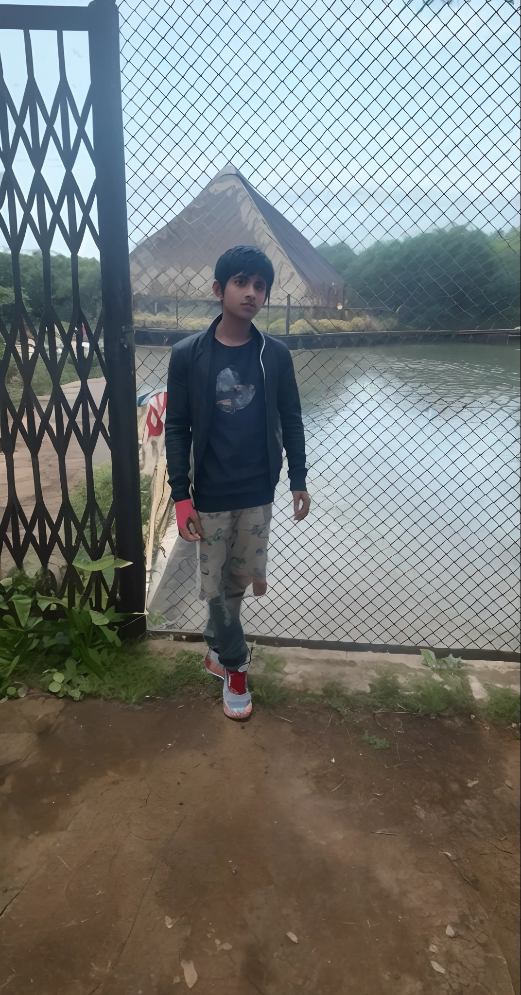 there is a young boy standing by a fence by a lake, very very low quality picture, in lake, full body picture, mohamed chahin style, connected with hanging bridge!!, scenary, old picture, around 1 9 years old, teenage boy, ayan nag, cool pose, riyahd cassiem, standing next to water, in a lake