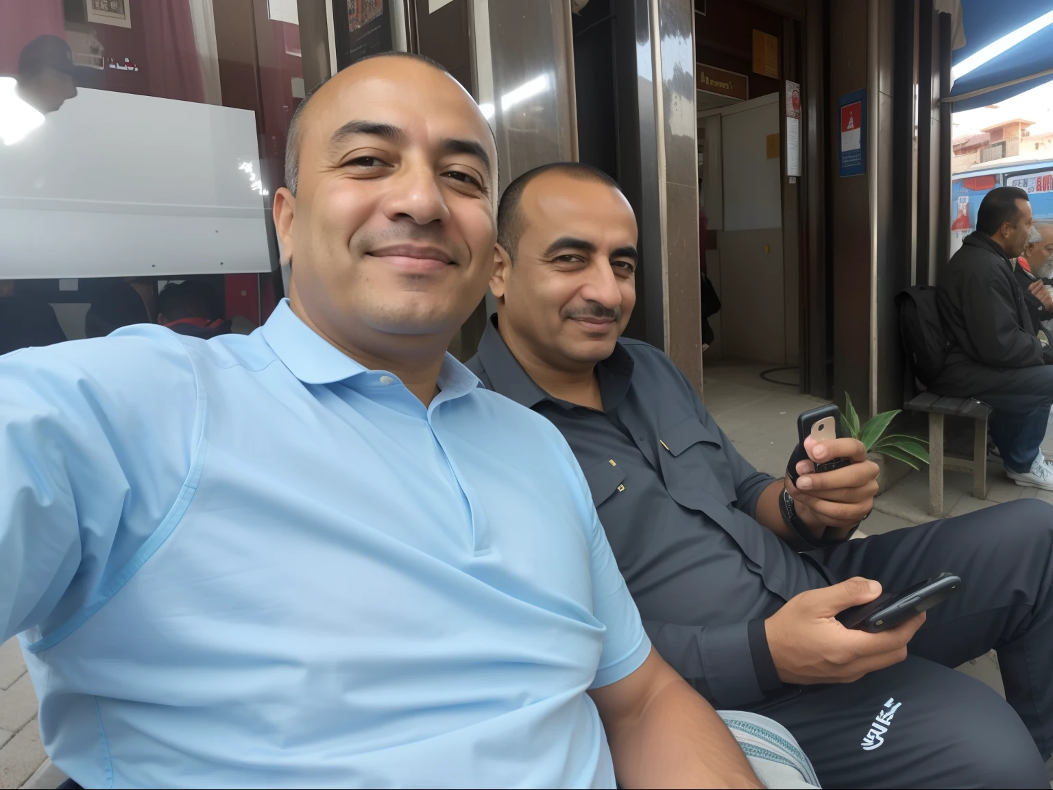 There are two men sitting on a bench with their mobile phones, Ayanamikodon et Irakli Nadar, Ghutra et Egal, very very low quality picture, from Egypt, in Egypt, Hommes de 45 ans, Dans City Street, Avec Godray, high quality image, Photo de profil, high picture quality, Photo prise en 2 0 2 0