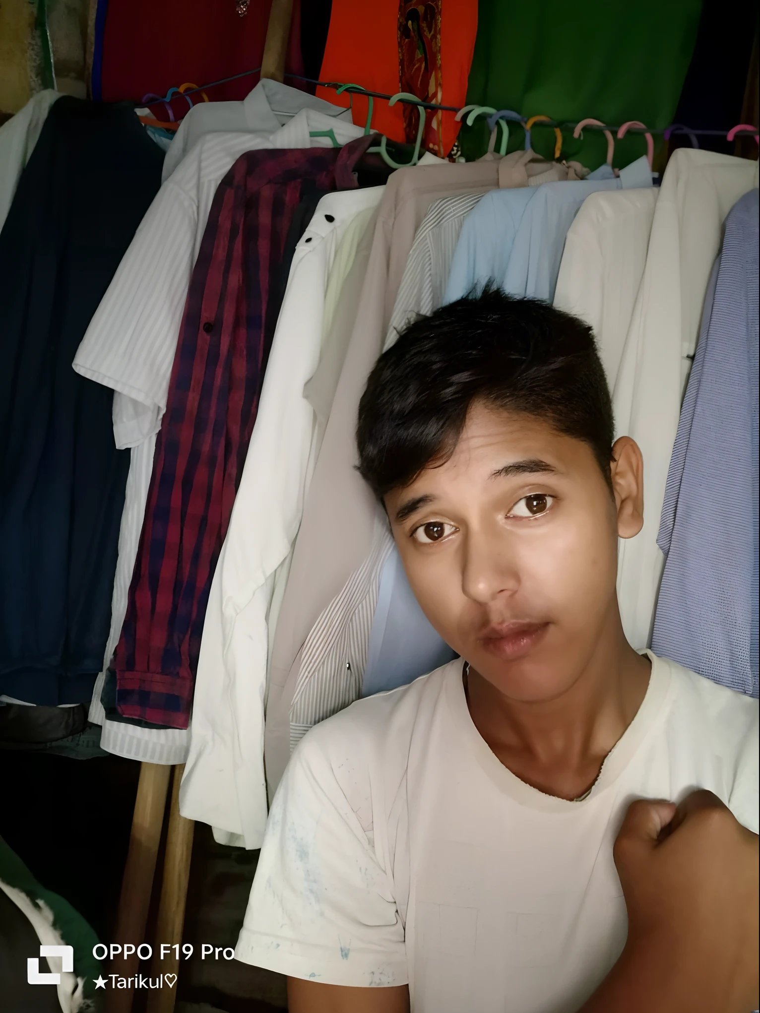 arafed man in front of a rack of shirts in a clothing store, with accurate face, with lovely look, wearing in shirt, with kind face, candid picture, in small room, around 1 9 years old, front profile!!!!, very very low quality picture, in tshirt, ayan nag, candid photo, selfie photo, good looking face, assamese aesthetic