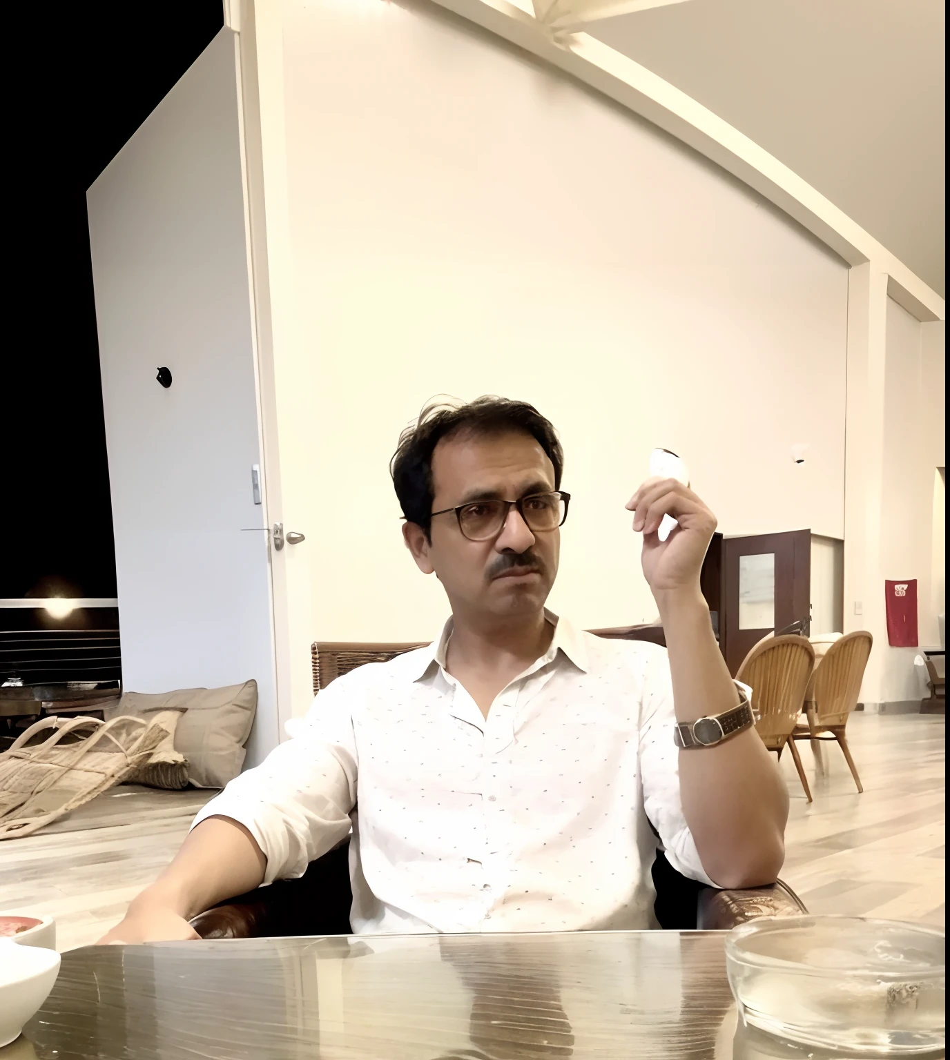 there is a man sitting at a table with a cup of coffee, mohamed chahin style, inspired by Bikash Bhattacharjee, sitting in a cafe, artistic pose, sitting in a cafe alone, very artistic pose, youtube video screenshot, low quality video, an artistic pose, candid picture, at night time, profile pic, with cigar, there is gun on table with godfather attitude in background there is stash of guns
