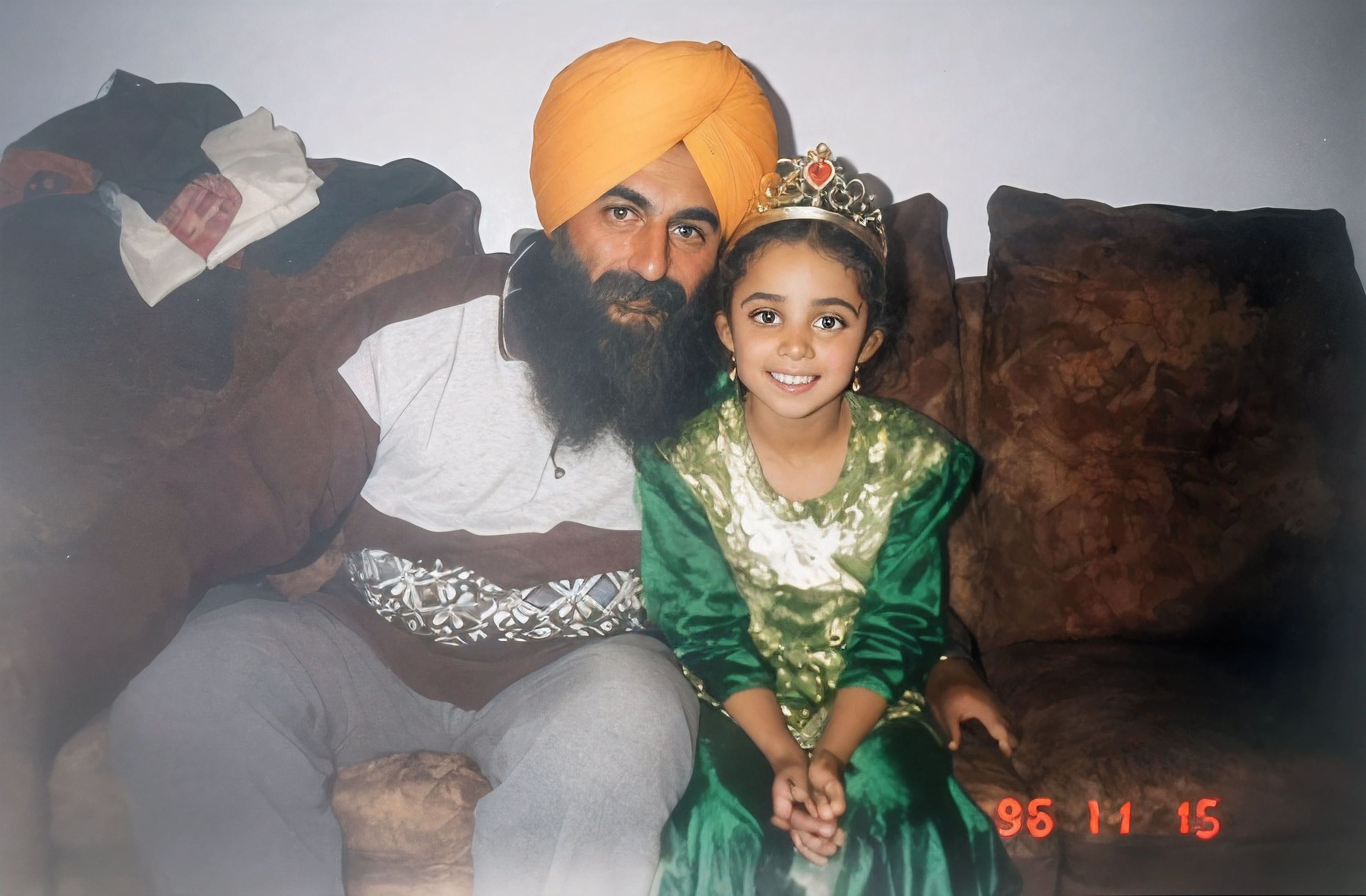 There is an Arab man and girl sitting on a sofa, tomada em 1 9 9 6, with a , homem com turbante laranja, olhos pretos, barba grande de cor preta, He has a white and brown tshirt and grey trousers, The girl has a crown on her head and wears a dark green dress with bright green in the center, raw photo, amazing photograph, best quality, 8K, high quality, Ultra detailed, (best quality), (high detailed skin, full sharp:1.2), 8k uhd, dslr, detailed face