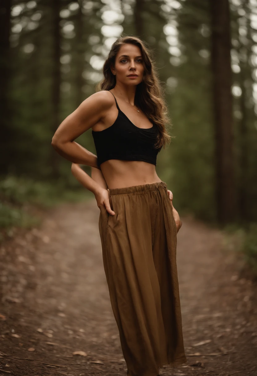 A woman standing in the woods wearing a black top and brown pants ...