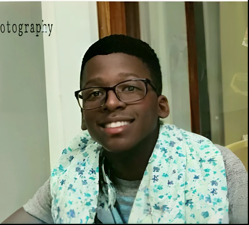 Homme souriant avec des lunettes et une écharpe assis à une table, Adolescent noir, David Uzochukwu, il a environ 20 ans, il a environ 2 0 ans, Photo tendance, Godwin Akpan, Photo découverte, prise au début des années 2020, Arik Roper, il a environ 2 5 ans, photo de l’album