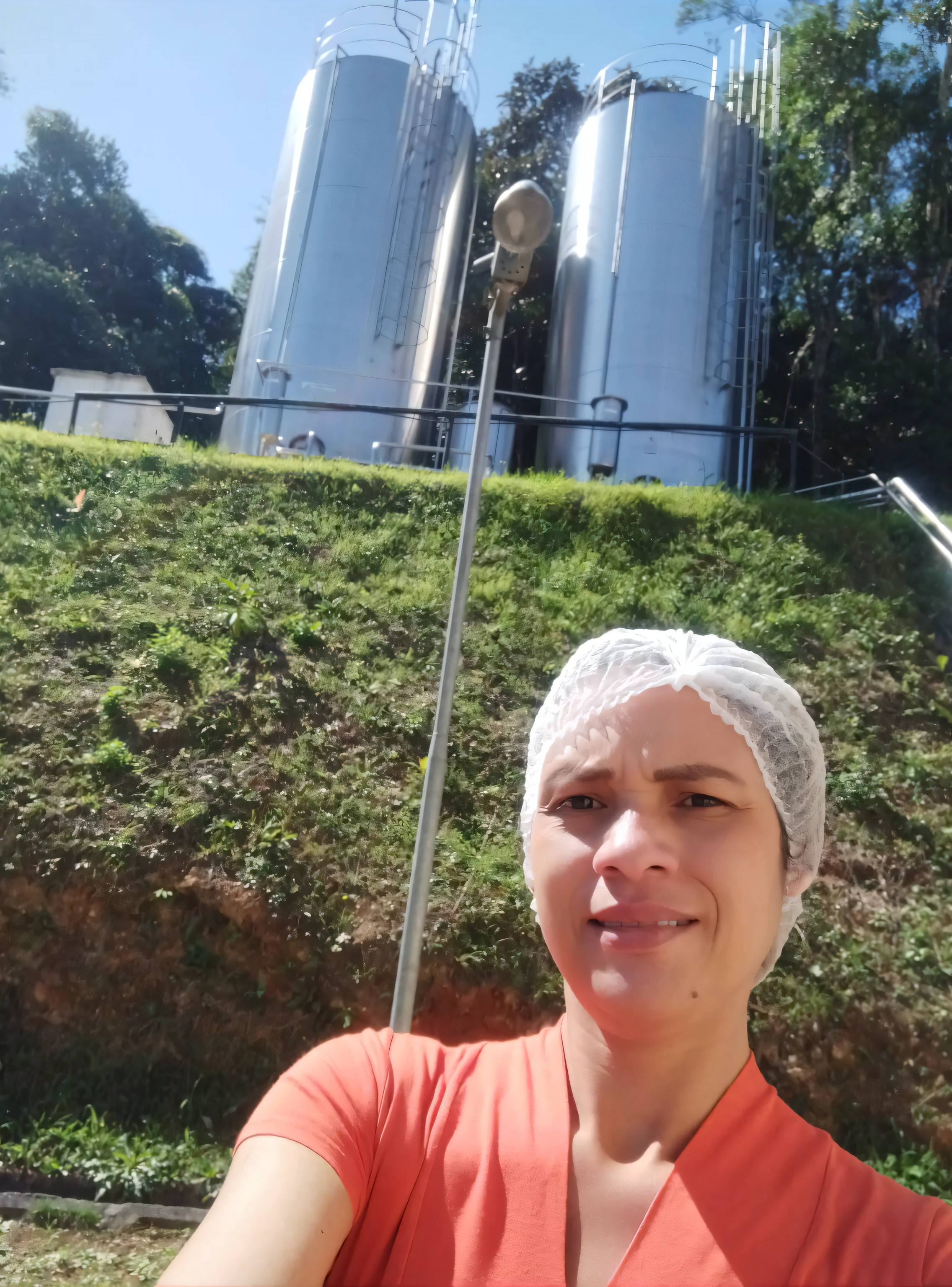 mulher tirando uma selfie em frente a um grande silos, com a terra ao fundo, com um parque ao fundo, com montanhas ao fundo, trabalho pioneiro suado e grosseiro, Colinas ao fundo, Malika Favre, Parque em segundo plano, 2 5 I, Minas Tirith ao fundo, 8 mil. preenchendo a maior parte da vista