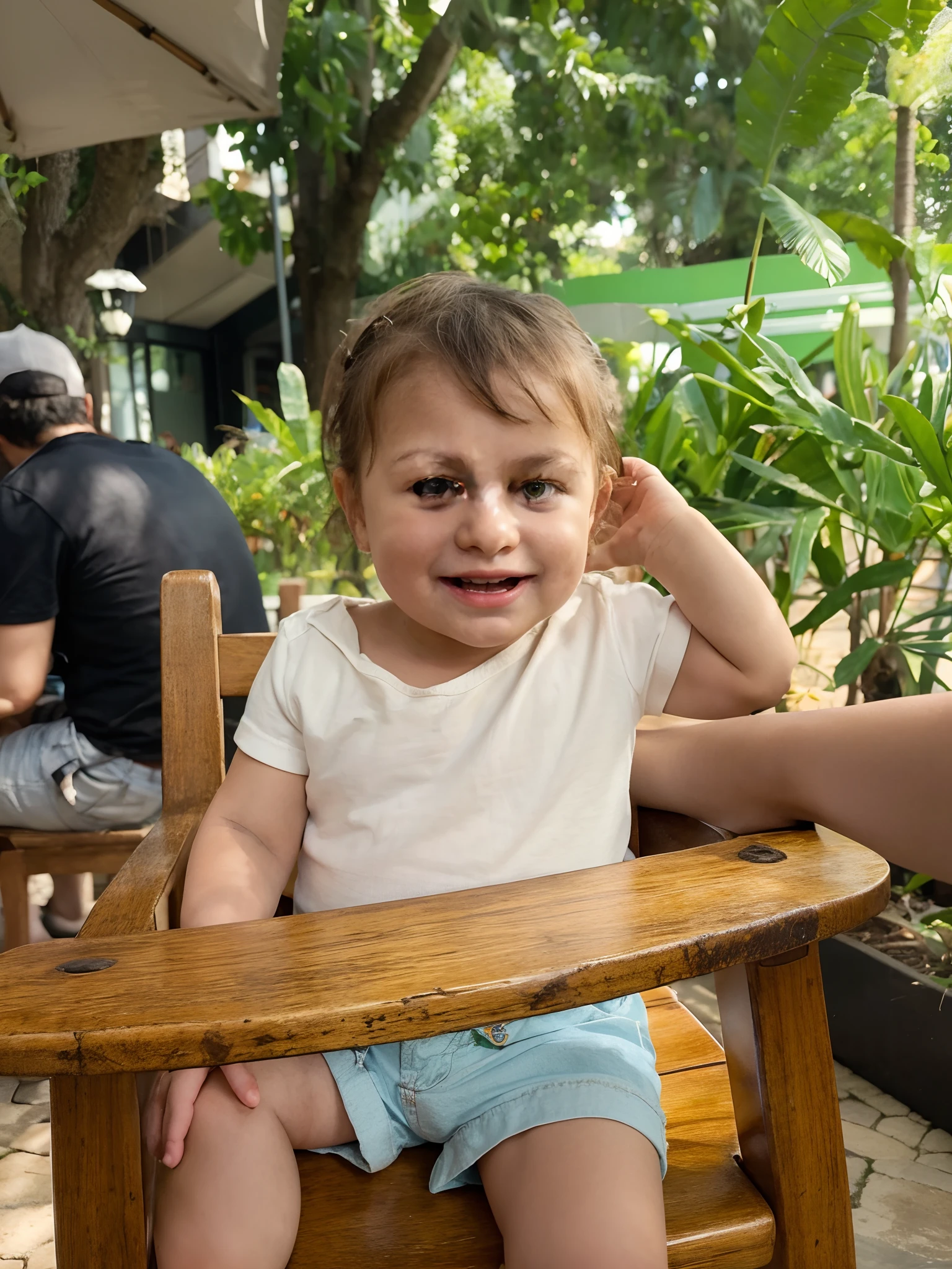 A baby sitting on a chair, com um sorriso no rosto e a mao na orelha