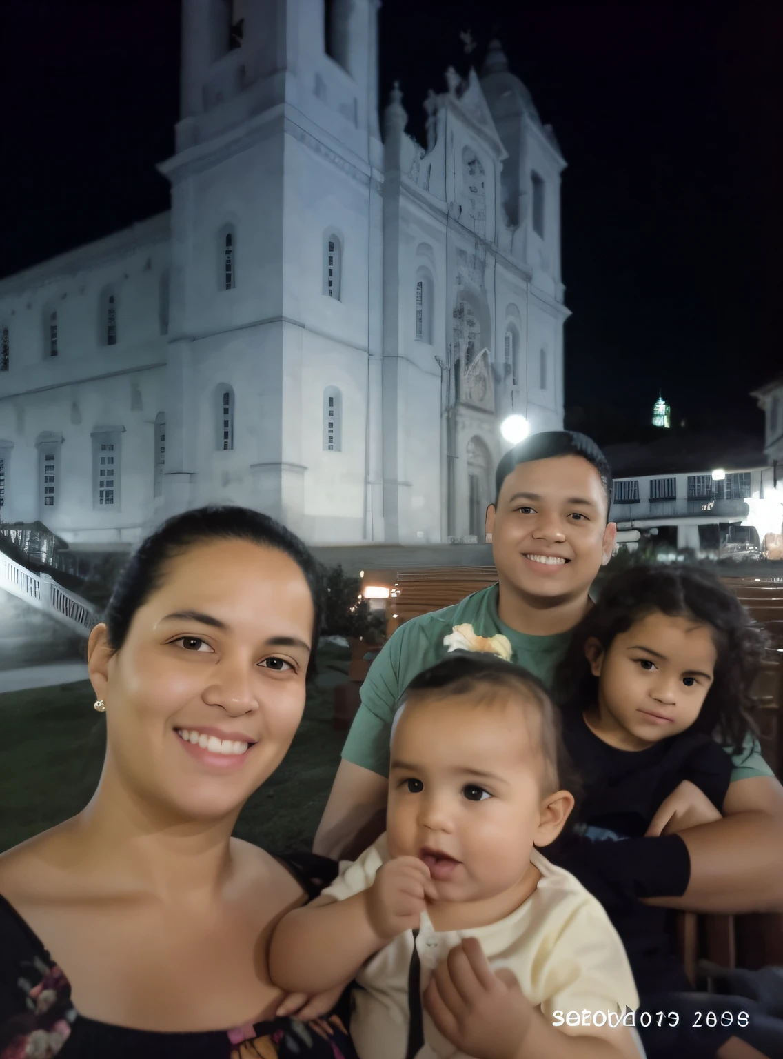Image with mother with daughter on her lap and father holding eldest daughter also on his lap with antique cathedral in the background