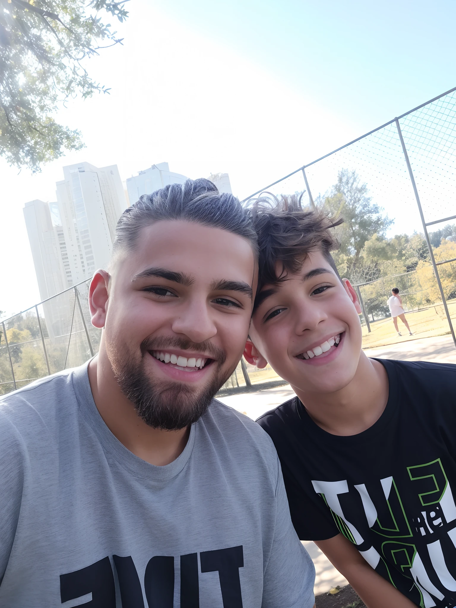 There is a man and a boy who are posing for a photograph in a park with many trees and a lake in the background. The boy is smiling and has hair with highlights and a nice topknot