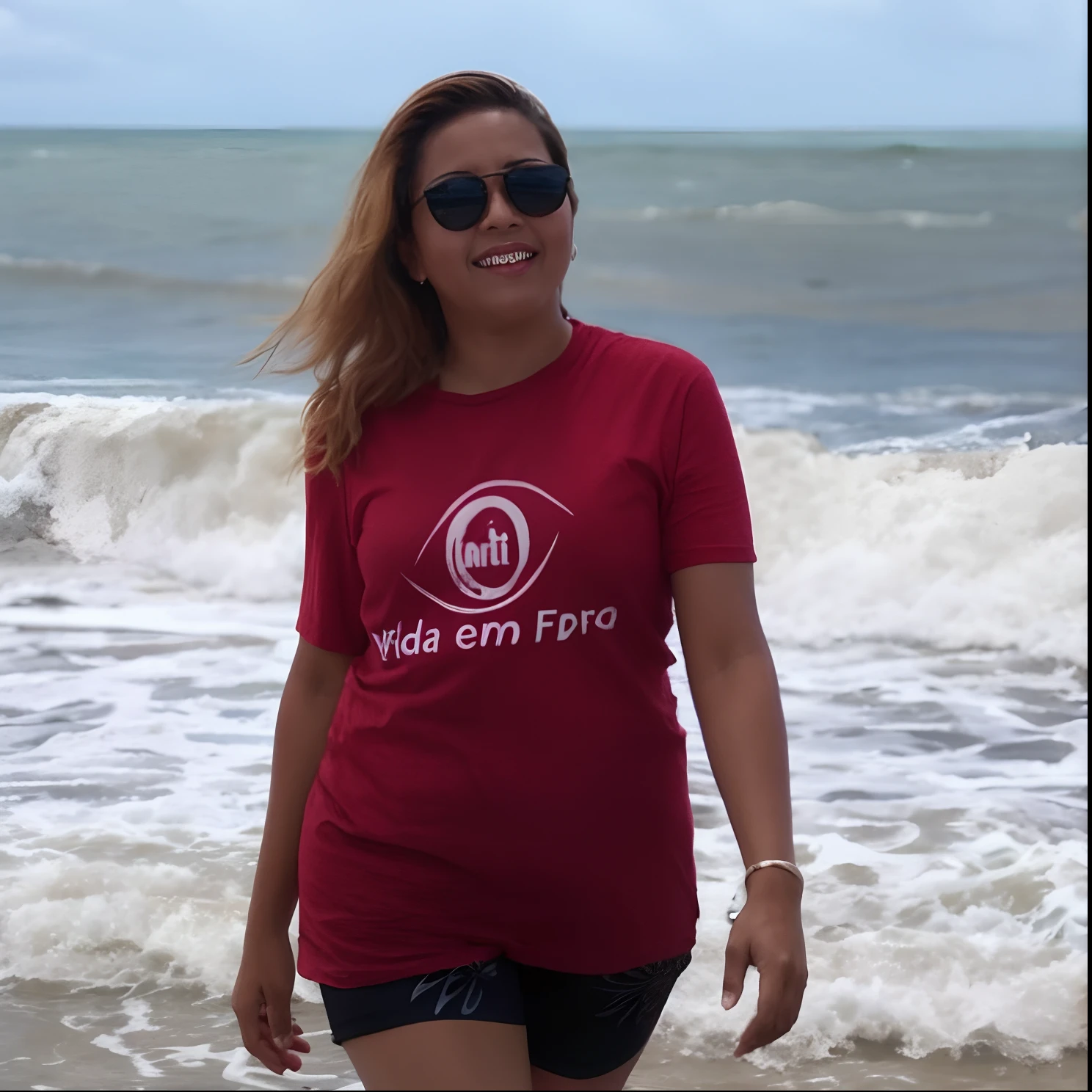 Smiling woman in red shirt standing on the beach next to the ocean, Directed by: Nandor Soldier, posando em uma praia com o oceano, andrea rocha, Caroline Gariba, Malika Favre, O oceano ao fundo, standing near the beach, na praia, standing at the beach, imagem de perfil, Marischa Becker, no oceano