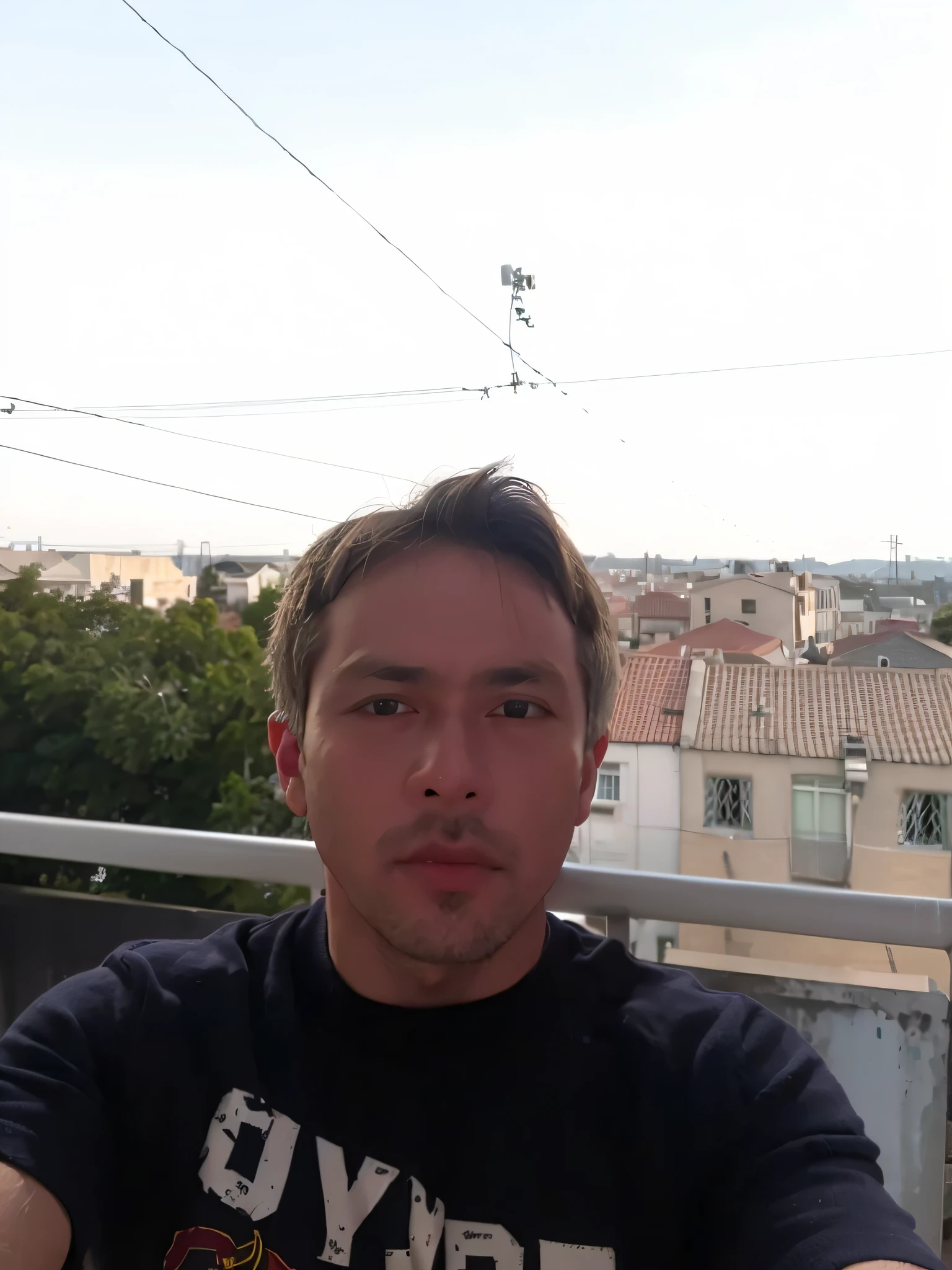 A man standing on a balcony with half body in the background of houses on the outskirts