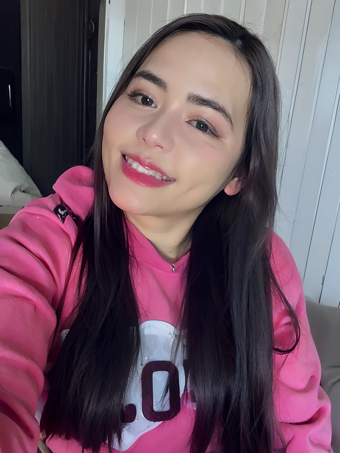 Uma mulher branca sorrindo com moletom rosa manga longa, cabelos e olhos castanhos.