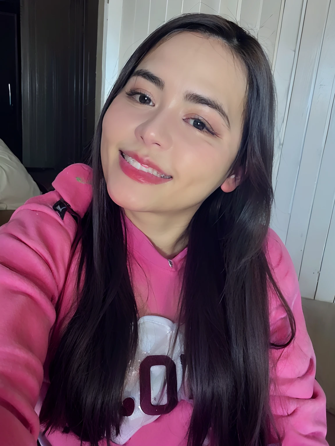Uma mulher branca sorrindo com moletom rosa manga longa, cabelos e olhos castanhos.
