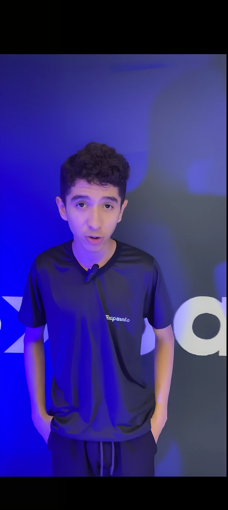 arafed boy in a black shirt standing in front of a blue wall, by Luis Miranda, emad mostaque, ismail, youtube thumbnail, by Jacob Pynas, performing, caio santos, solid background, by Samuel Silva, mohamed chahin style, asher duran, by David Ruby, by Dan Content, youtuber, saadane afif