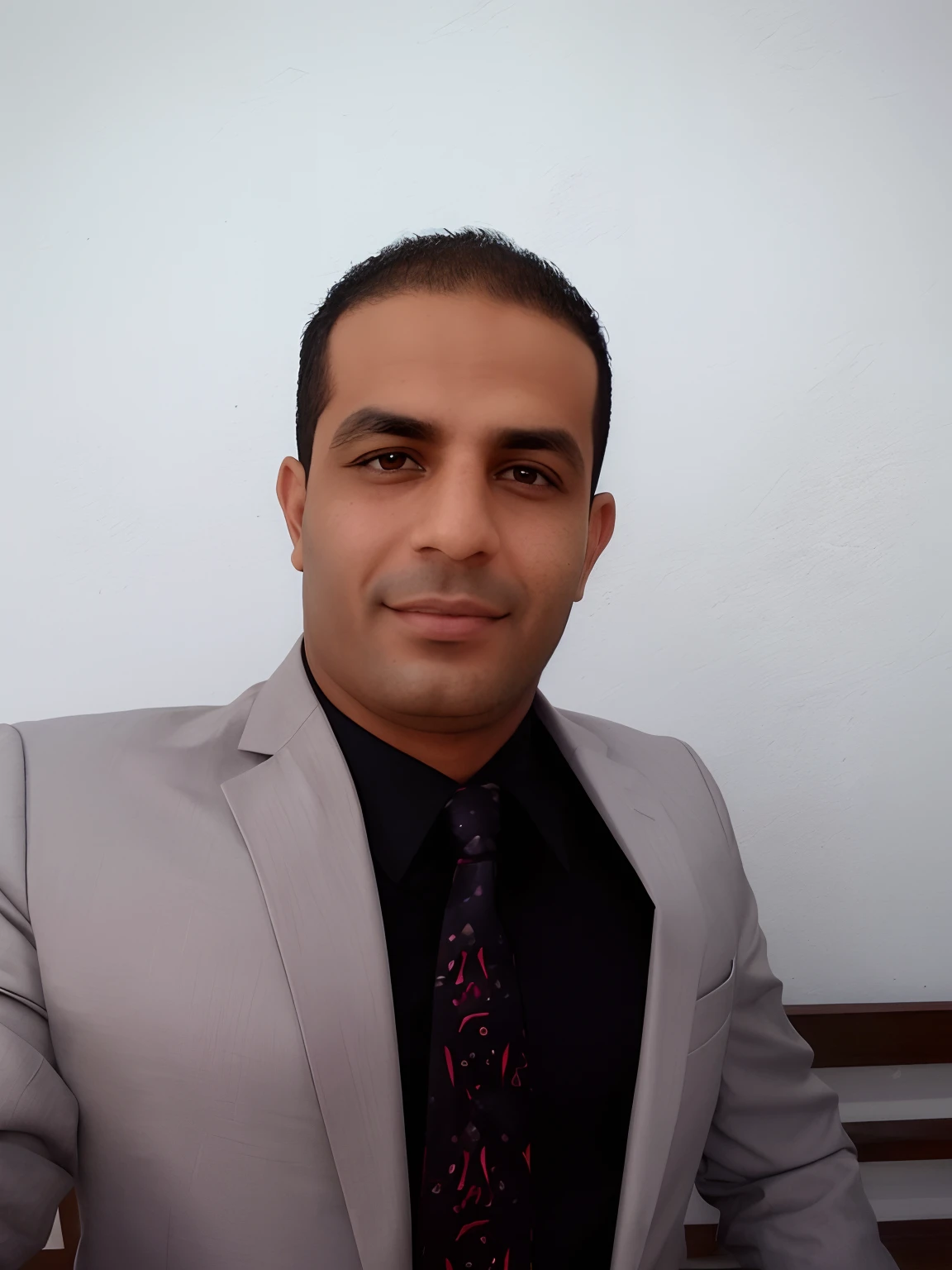 homem sorridente em um terno cinza e camisa preta sentado em um banco, Mohamed Chahin, Ahmad Merheb, Amr Elshamy, Mohamed Reda, Emad Mostaque, Sam Nassour, Hicham Habchi, Eytan Zana, Jamel Shabbaz, Farid Ghanbari, Advogado curdo, Saadane AFIF, andres rios