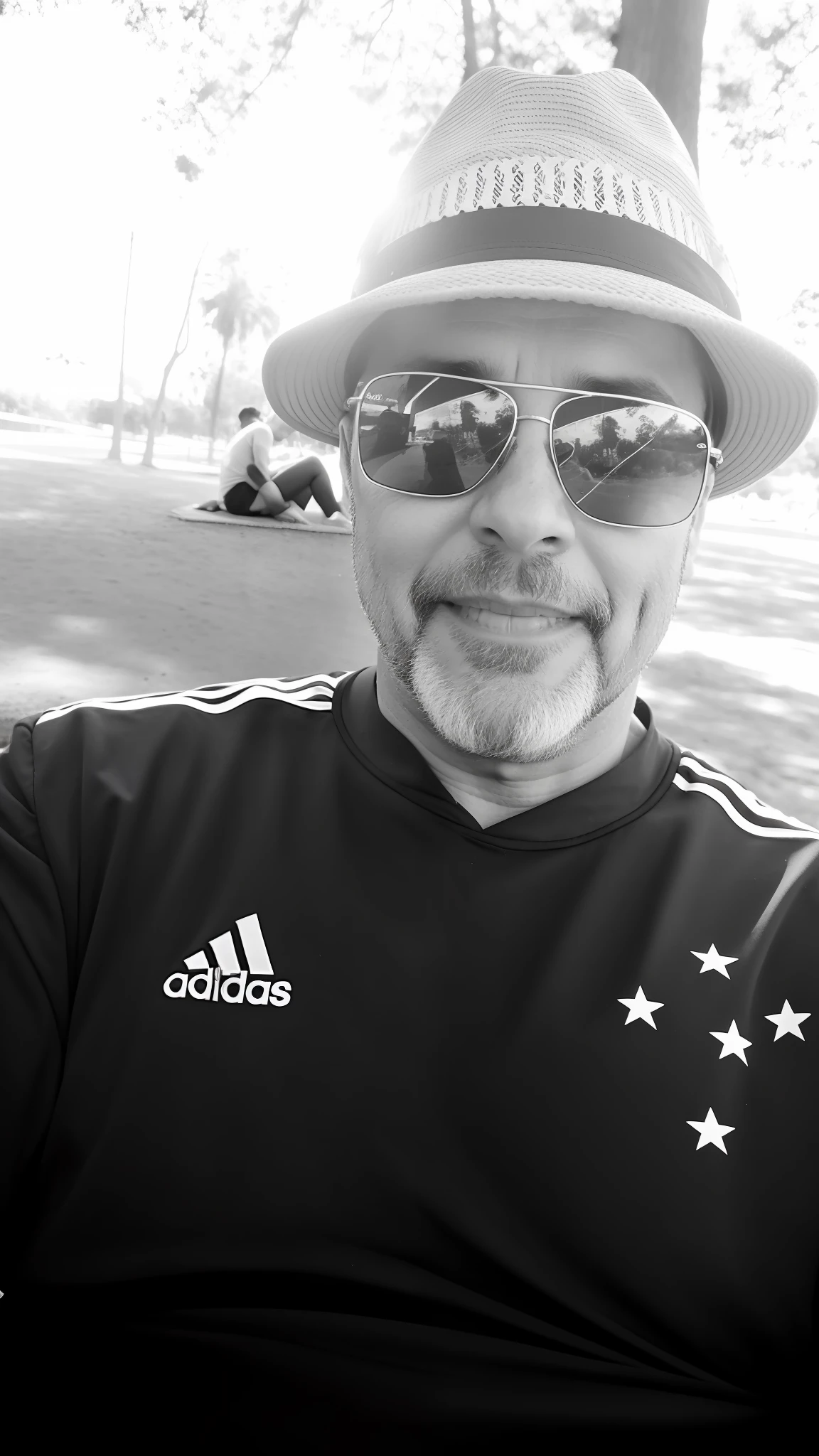 There's a man wearing a hat and sunglasses sitting in a park, relaxing after a hard day, em um parque, usando roupas adidas, ele tem cerca de 40 anos, ele tem cerca de 4 0 anos de idade, Tiro no iPhone 6, ele tem cerca de 5 0 anos de idade, ele tem cerca de 50 anos, inspired by Nuno Gonçalves