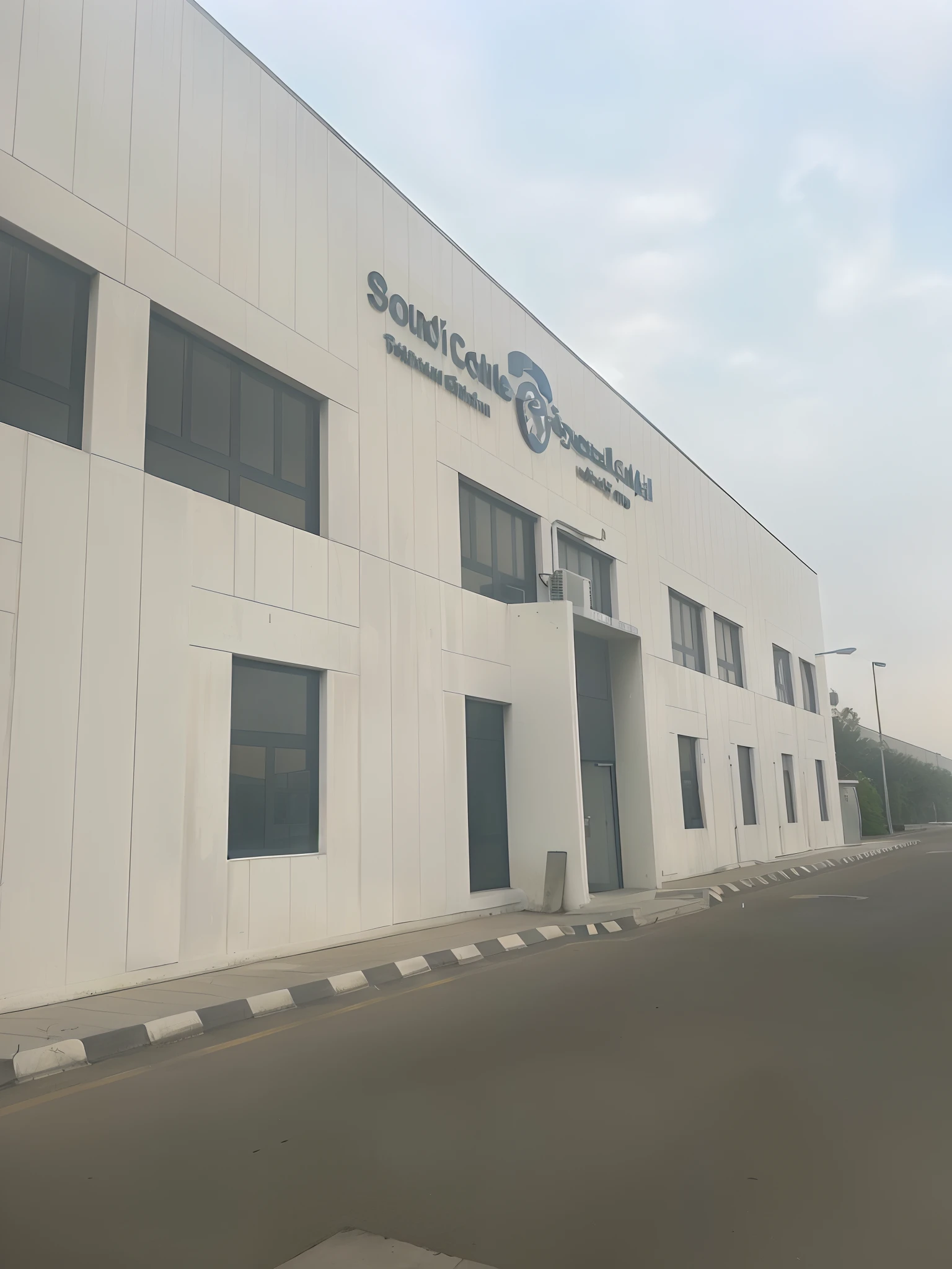 there is a white building with a sign on the side of it, centre image, building facing, private academy entrance, picture taken from the ground, medical research facility, medical complex, office building, research complex, research center, wide angle exterior 2022, outside view, modern technology building, photo taken from the ground, sand storm enters stone