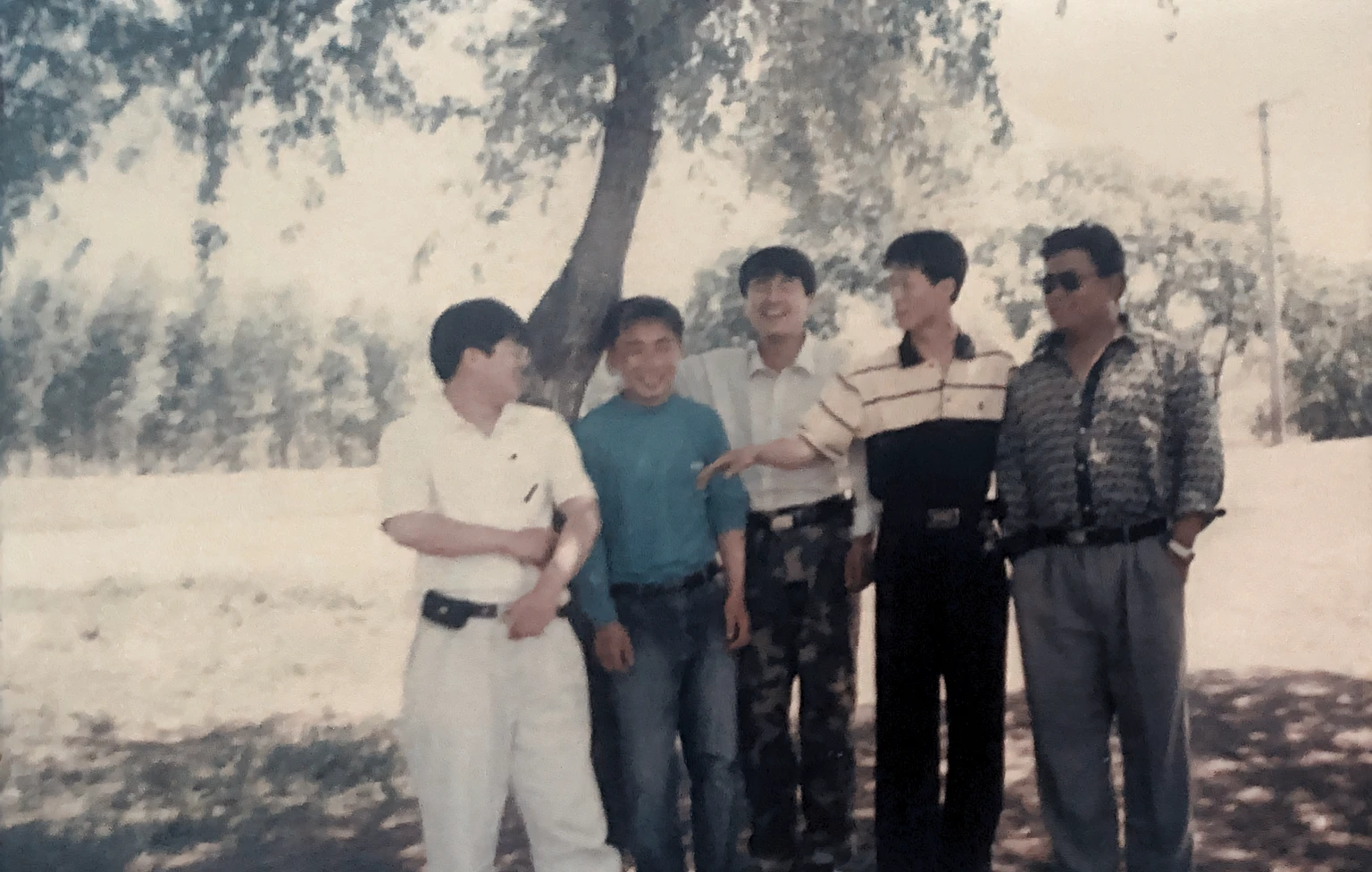 There are many men standing together under a tree in the park, photo from the 80s, around 1 9 years old, in 1 9 8 5, taken in the late 1980s, scanned in, taken in the early 1990s, 80's japanese photo, photo 1 9 9 0 s, about 3 5 years old