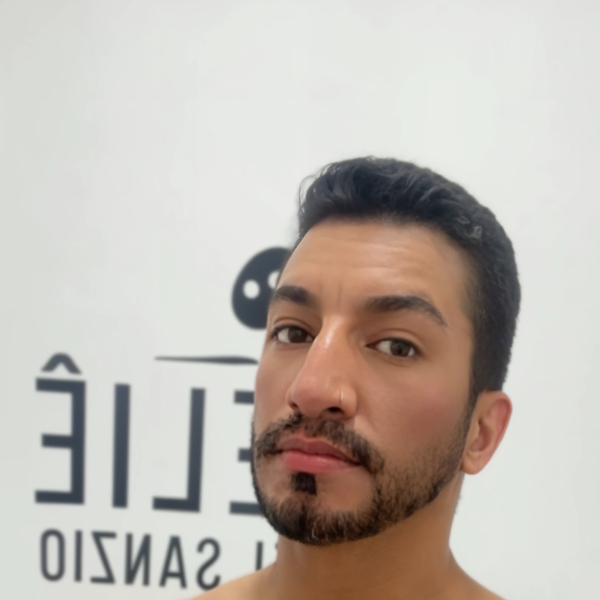 dark-skinned man, brown eyes, short hair, low beard, with tattoo on his left arm.