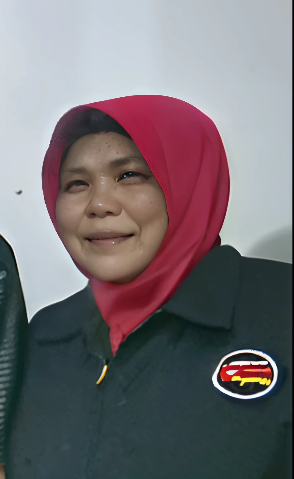 A 50 year old Indonesian woman, wearing a red hijab and black jacket, smiling, with brown skin