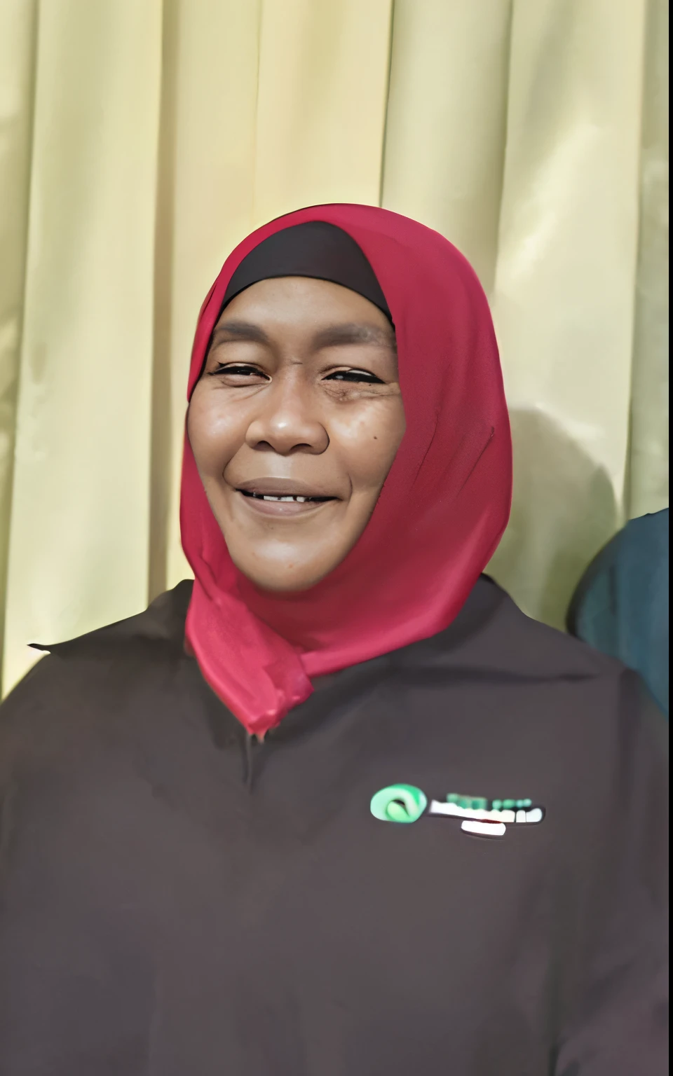 A brown-skinned woman wearing a red hijab, smiling, eyes looking forward