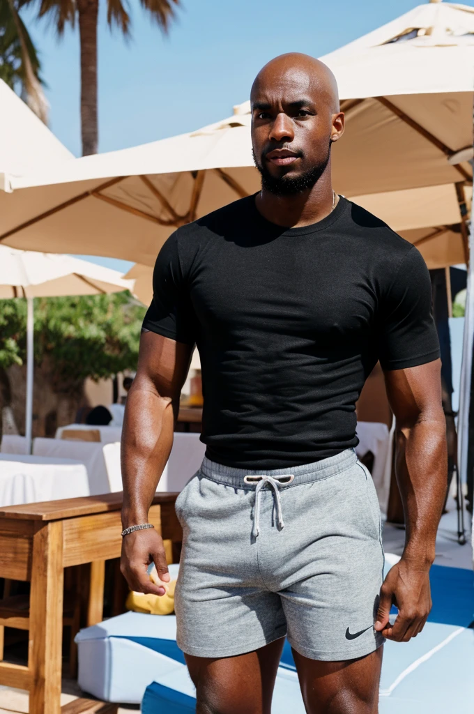 26 year old black guy mathys with muscles and bald head wearing a tshirt and shorts in a ibiza beach club