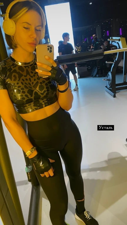 The woman, who takes a selfie in the mirror, in the gym in latex, taken in Latex Pic, Skinny, tight latex outfit, Black latex leggings,Latex crop shirt and strong abs,female model, tight fit, latex transparent, press in latex