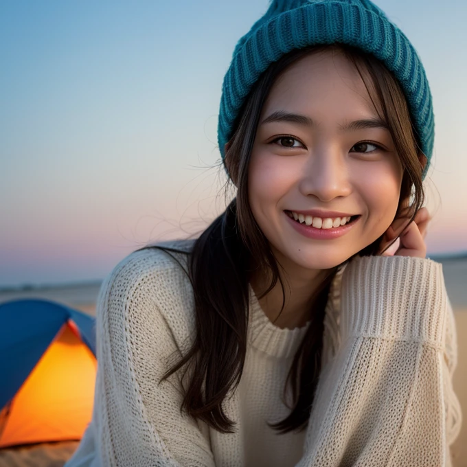 Create an image of a young East Asian woman with a joyful expression, sitting in front of a camping tent on a sandy beach at dusk. She is wearing a cozy, casual white sweater and a warm brown beanie. Her hands are playfully framing her face as she smiles. The scene captures the relaxed atmosphere of a beach camping trip, with soft evening light that creates a tranquil and inviting mood