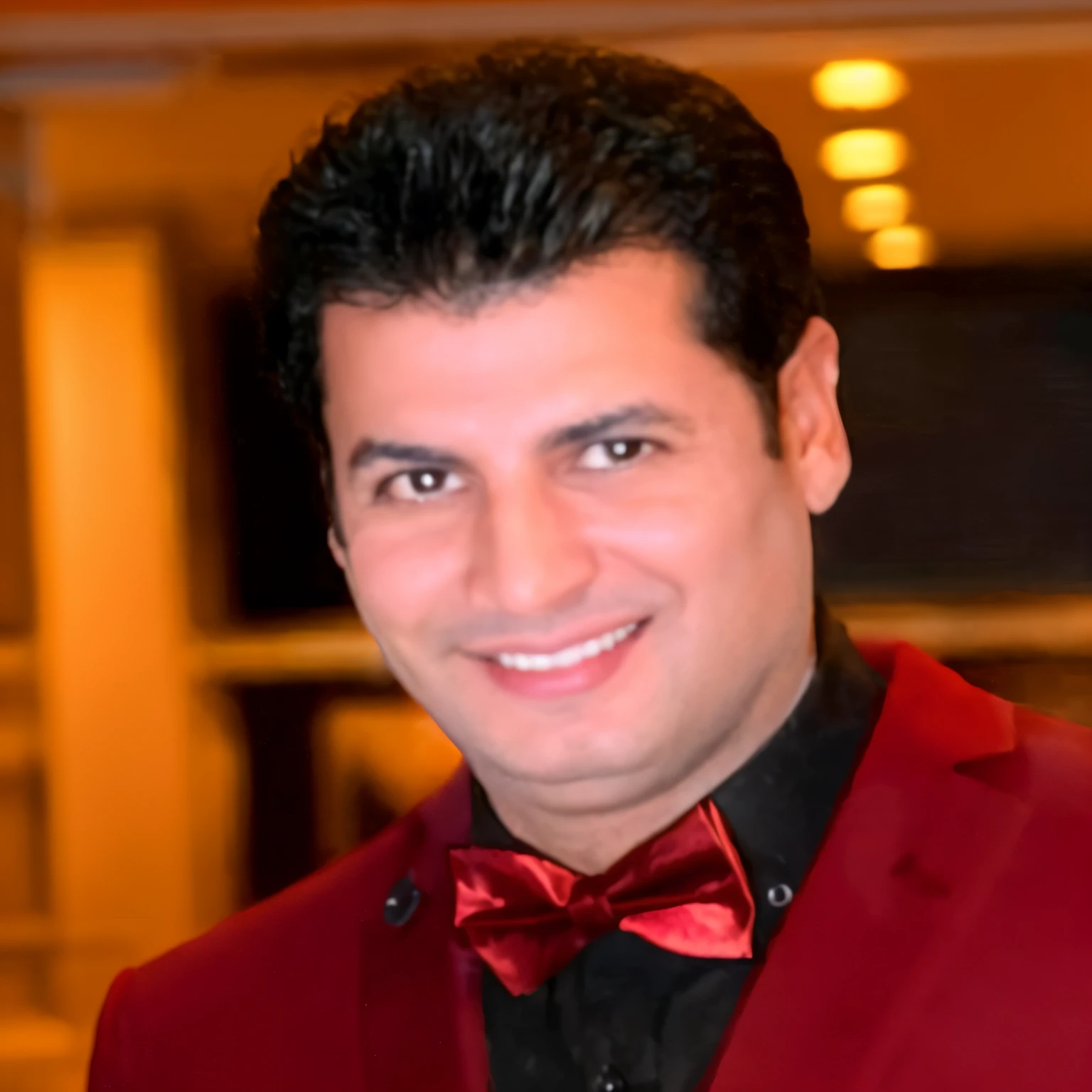 smiling man in red suit and bow tie standing in a room, ahmad merheb, eytan zana, mohamed chahin, amr elshamy, sam nassour, farid ghanbari, hicham habchi, sayem reza, enes dirig, richard taddei, jamel shabbaz, mohamed reda, nekro petros afshar