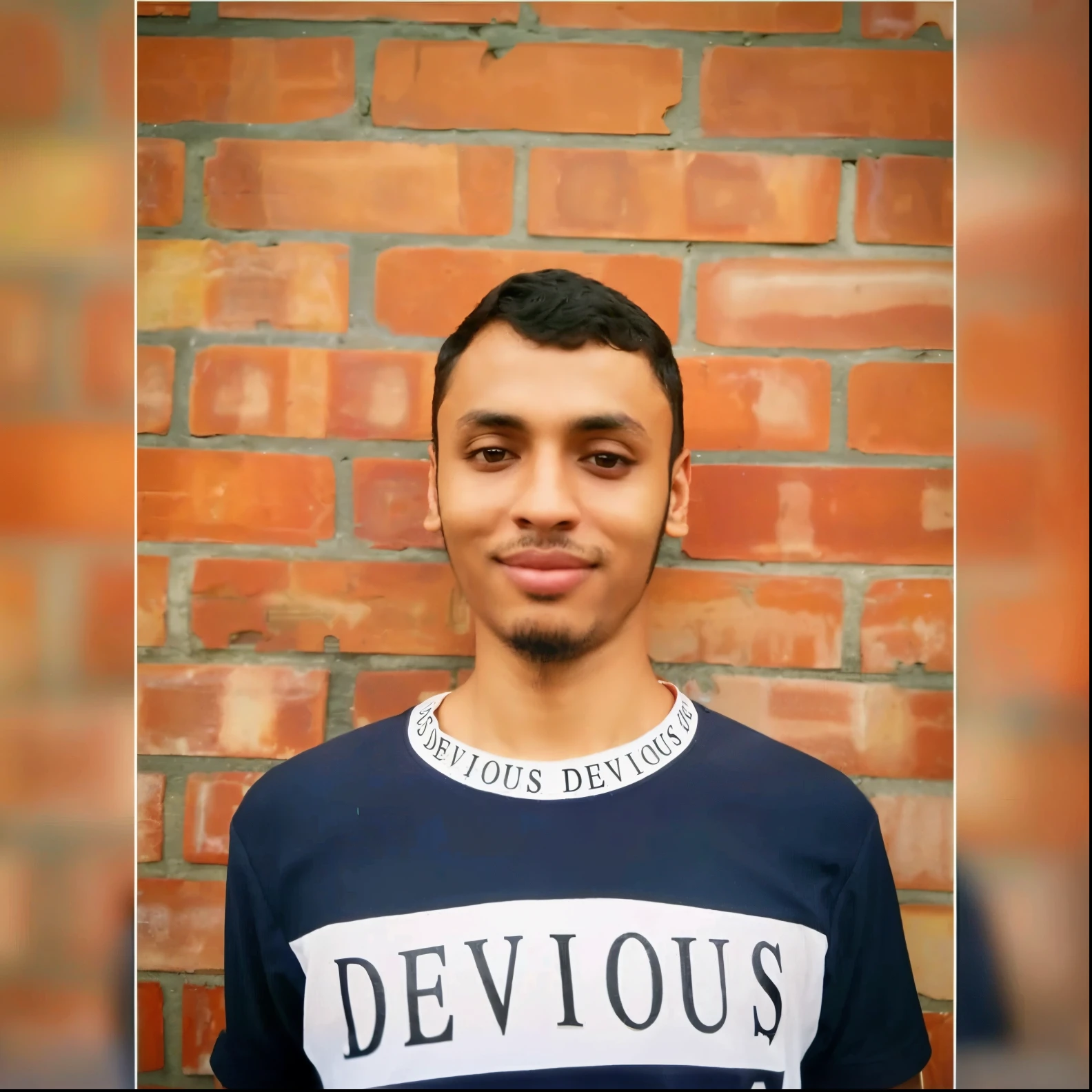 arafed man in a blue shirt standing in front of a brick wall, jayison devadas, riyahd cassiem, around 1 9 years old, facebook profile picture, old picture, profile pic, frontal picture, facebook post, portait photo profile picture, devious, devious evil expression, front profile!!!!, reyyan, proud serious expression