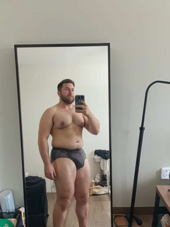 There is a thick obese hairy fat man taking a selfie and reaching his hands into his underwear