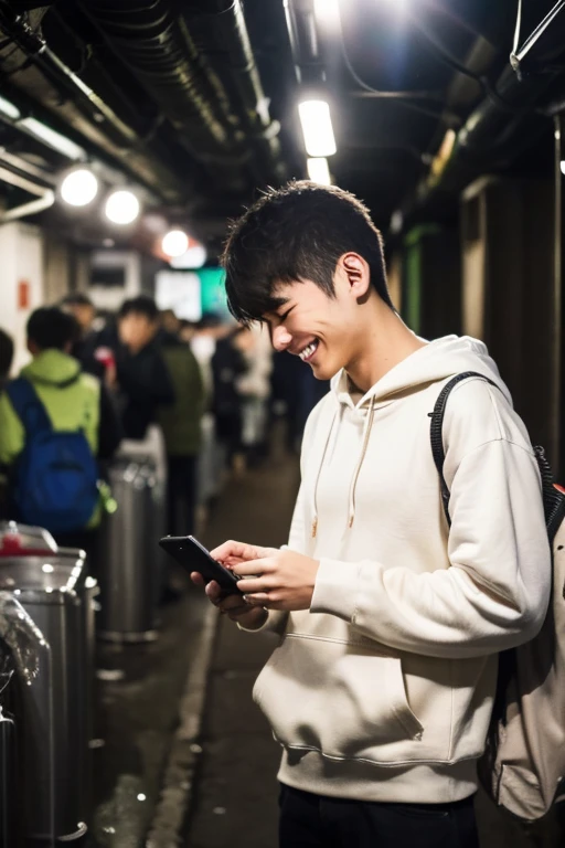 A 20-year-old Japanese man smiles while looking at his smartphone.,There are a lot of people in the underground live venue.,Wearing a white hoodie