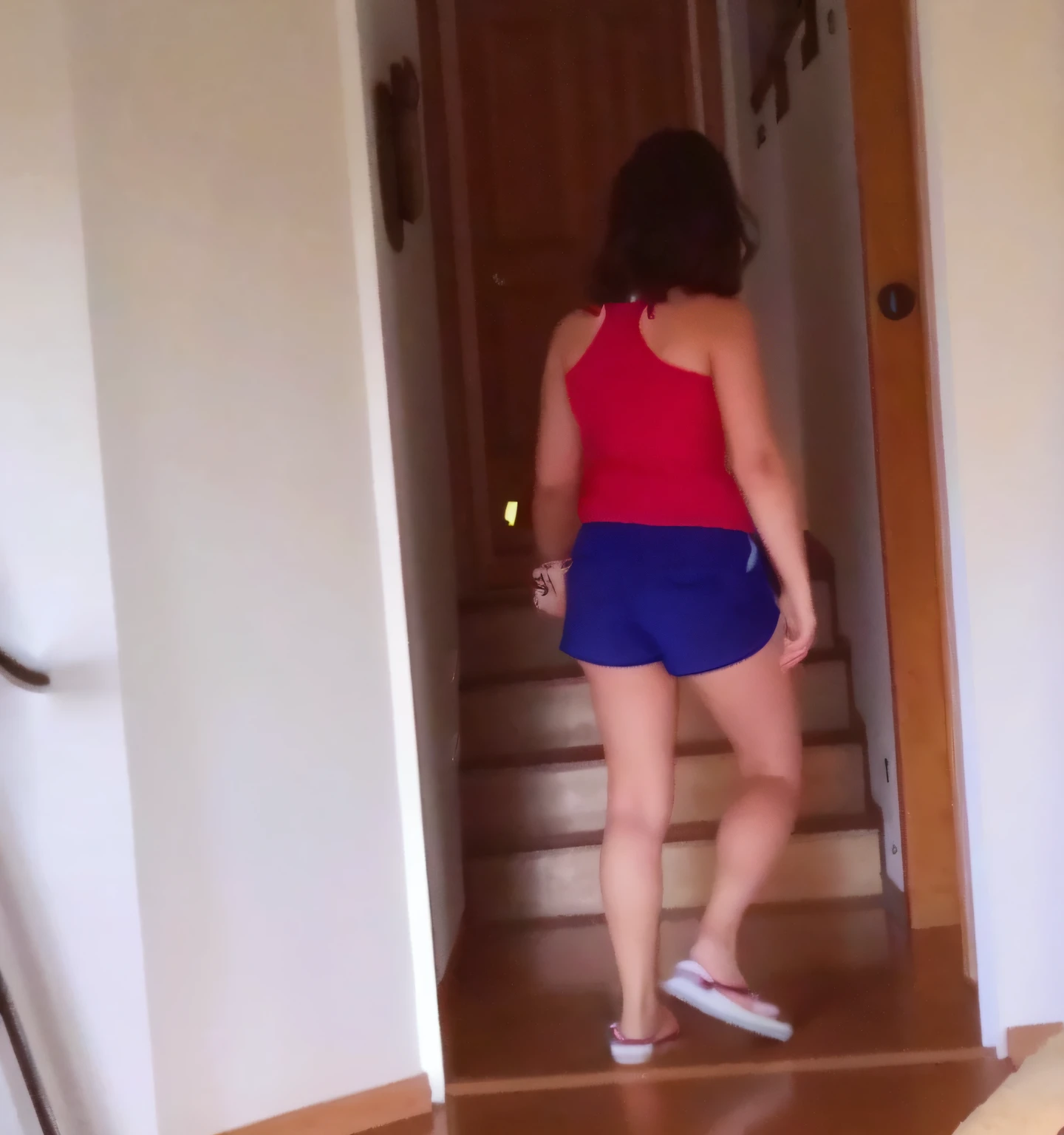 there is a woman walking down a flight of stairs in a house, side view of her taking steps, vestindo shorts vermelhos, Bermuda, descendo as escadas, vestindo camisola e shorts, view of the back, vestido com um top e shorts, walking away from camera, walking away from camera, seen from back, vestindo regata e bermuda