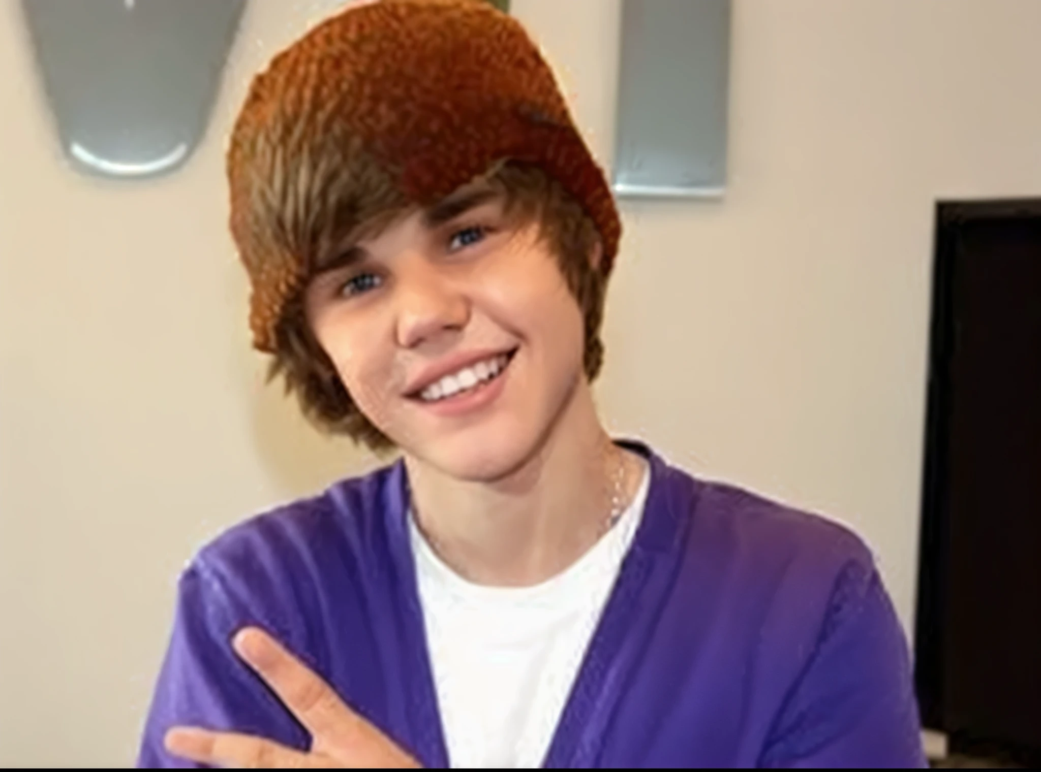 Justin Beiber holding up "i love you" sign language in room. Christmas Stocking hat., gray under armor shirt, blue eyes, brown hair.
