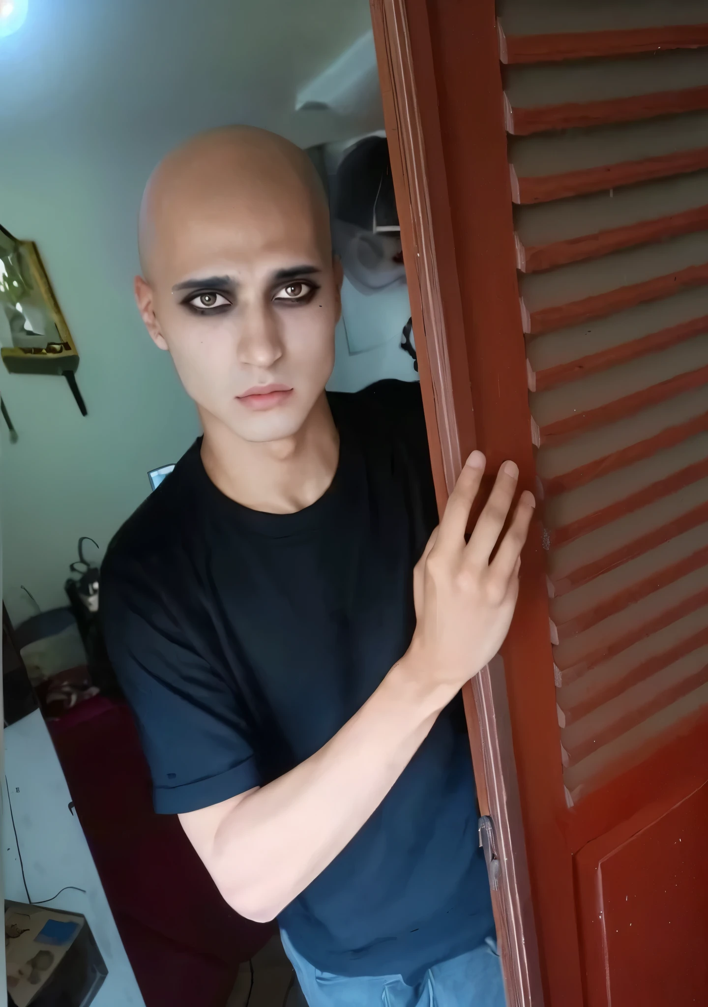 arafed man with bald head and black eye make up peeking out of a door, scary look, 1 7 - year - old boy thin face, with black sclera eyes, shaven face, emaciated shaved face, black eyes and large forehead, shaved face, heavy make up, showing forehead, heavy makeup, shaved head, buzzed hair on temple