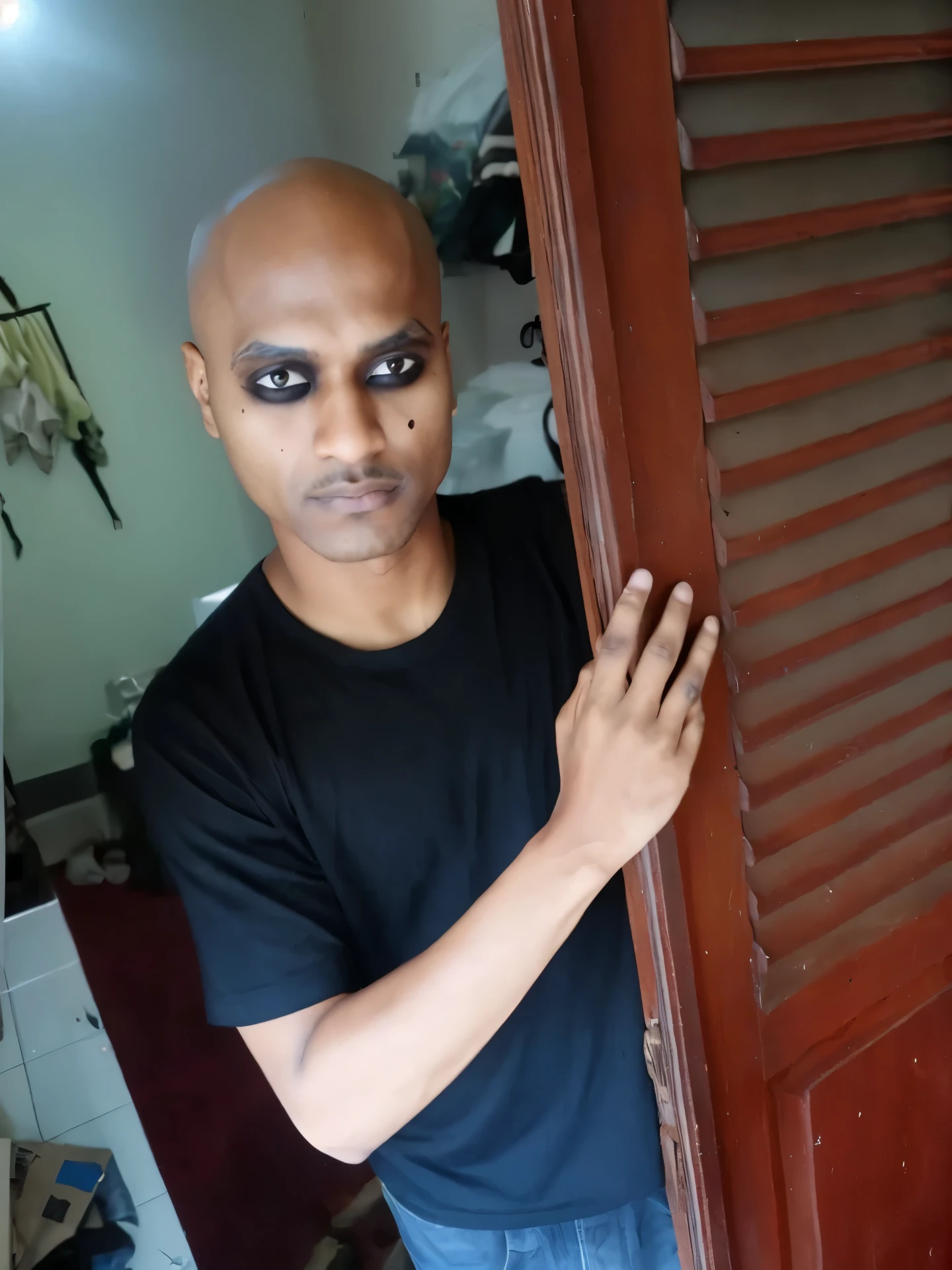 arafed black Asian man with bald head and black eye make up peeking out of a door, scary look, 1 7 - year - old boy thin face, with black sclera eyes, shaven face, emaciated shaved face, black eyes and large forehead, shaved face, heavy make up, showing forehead, heavy makeup, shaved head, buzzed hair on temple, very dark skin, very small eyes,