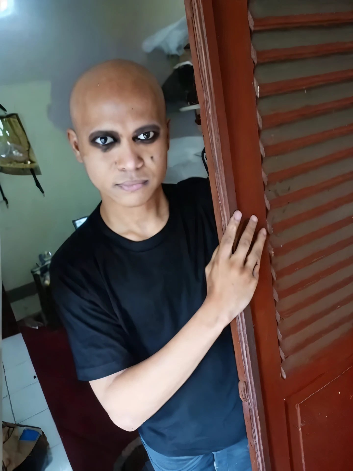 arafed black African man with bald head and have a cat ears, black eye make up peeking out of a door, scary look, 1 7 - year - old boy thin face, with black sclera eyes, shaven face, emaciated shaved face, black eyes and large forehead, shaved face, heavy make up, showing forehead, heavy makeup, shaved head, buzzed hair on temple, very dark skin, very small eyes, ((very small eyes)) ((cat ears))